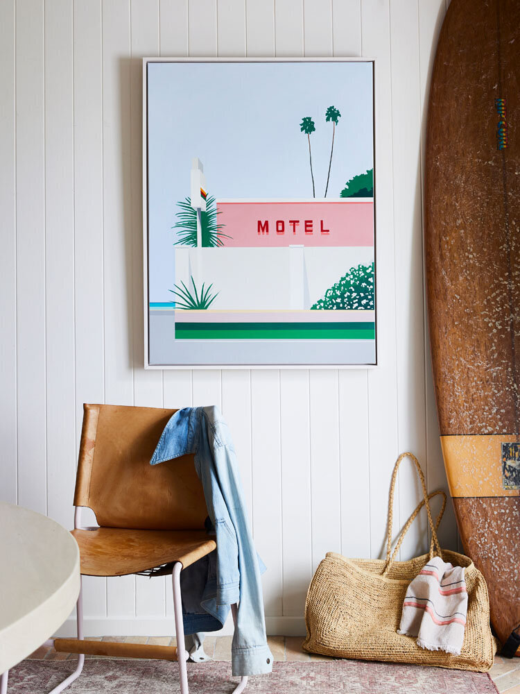 A casual living space with a large framed print of a retro motel sign with palm trees and a bright pink wall.