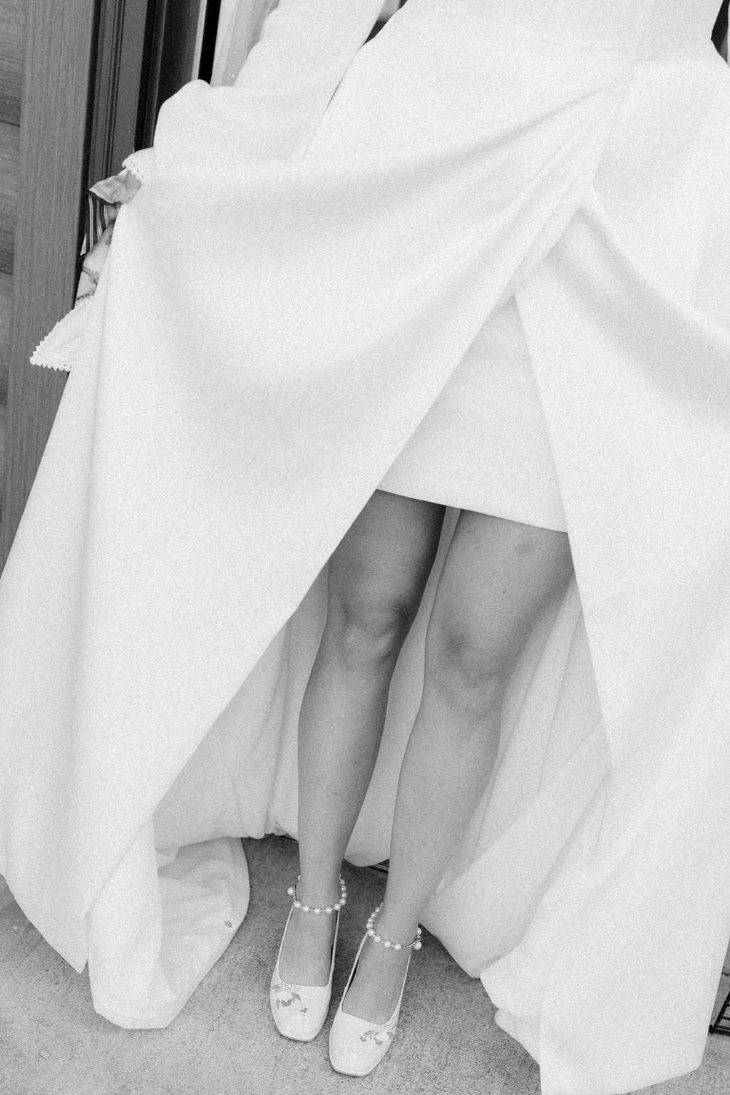 black and white photo of a wedding dress falling around a brides shoes