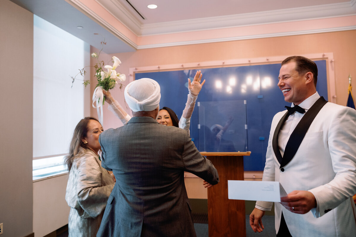 Bride Japna throws her hands up in celebration while hugging family after the City Hall wedding, as Chris smiles beside them