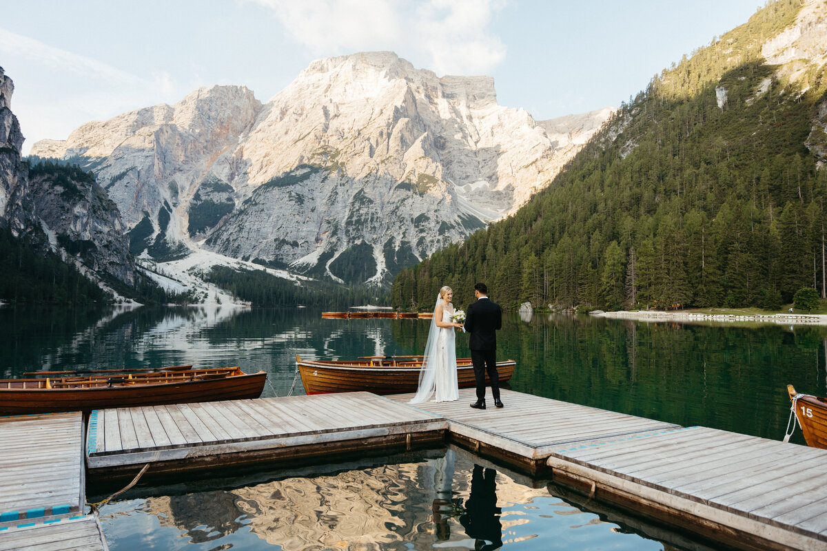 Bride walking toward groom on wooden dock at lake