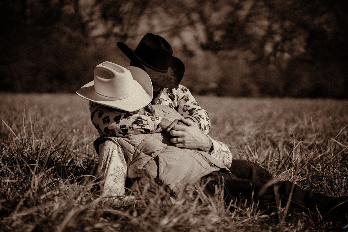 A same sex cowboy couple pose in a horse field in Tennessee in mismatched cowboy hats.