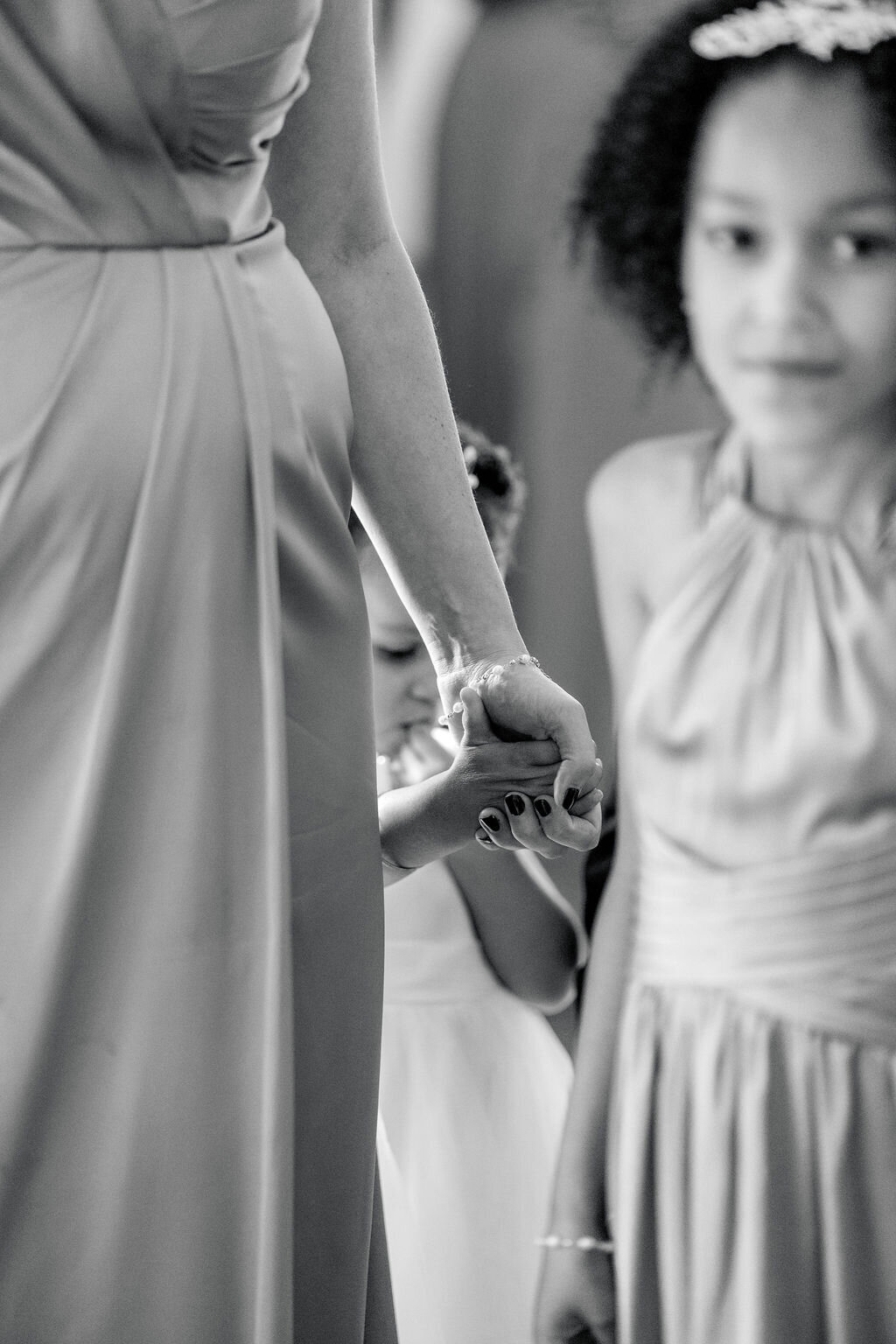 Wedding Photographer RI | Black and white image of a woman holding hands with a young girl, both in elegant dresses. Another child observes.
