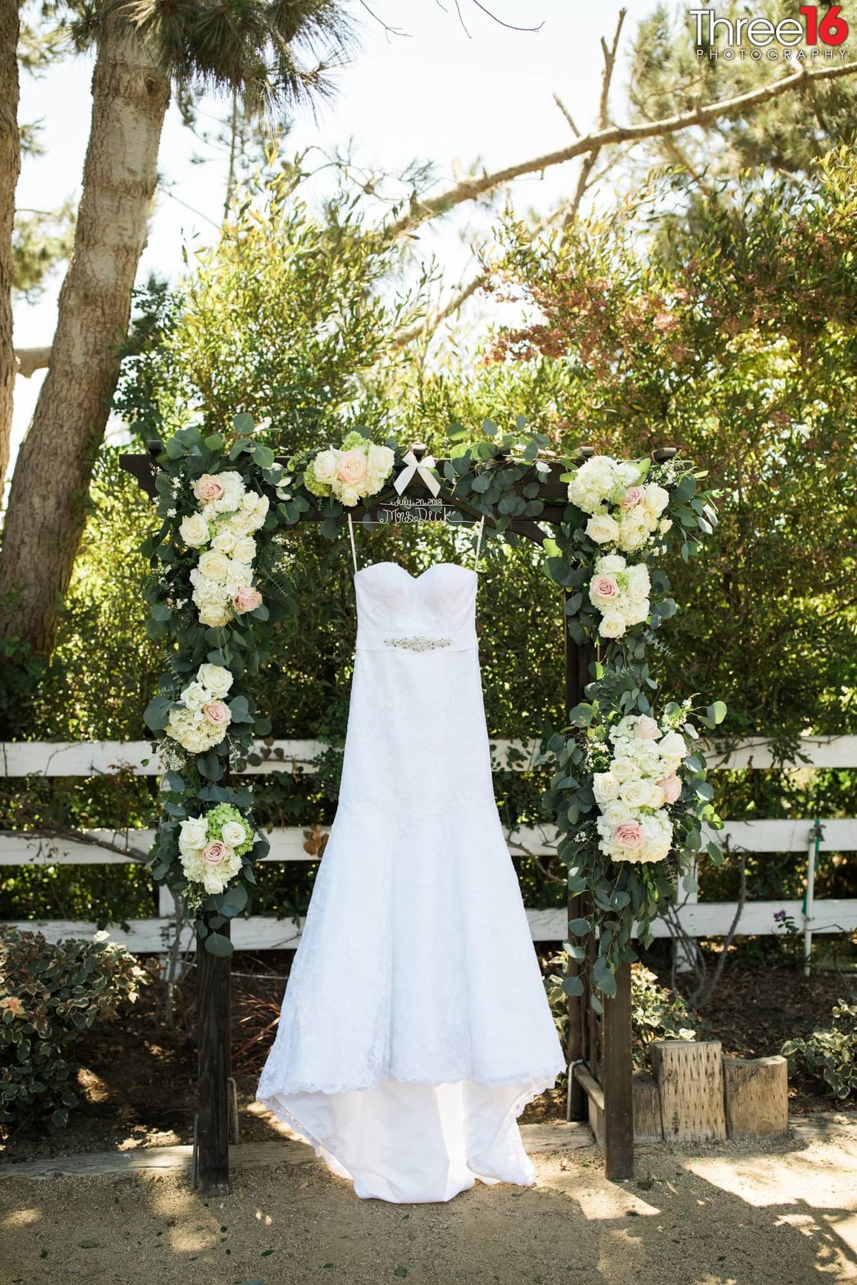 Bride's wedding dress hangs from a floral archway