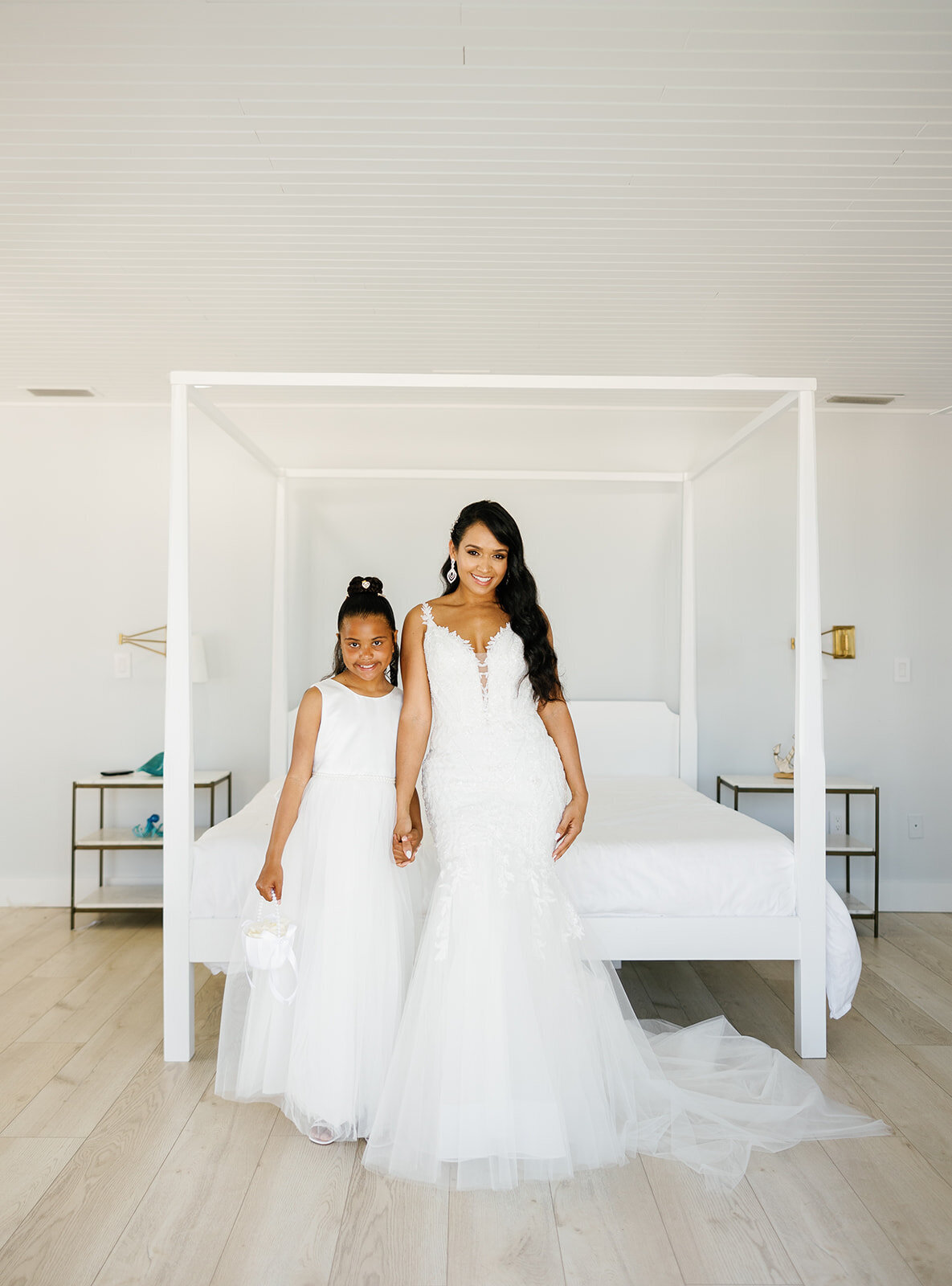 Andressa shares a heartfelt moment with her junior bridesmaid in matching white dresses, posing in a minimalist bridal suite at Table Key, Islamorada. Photography by Claudia Amalia Wedding Photography.