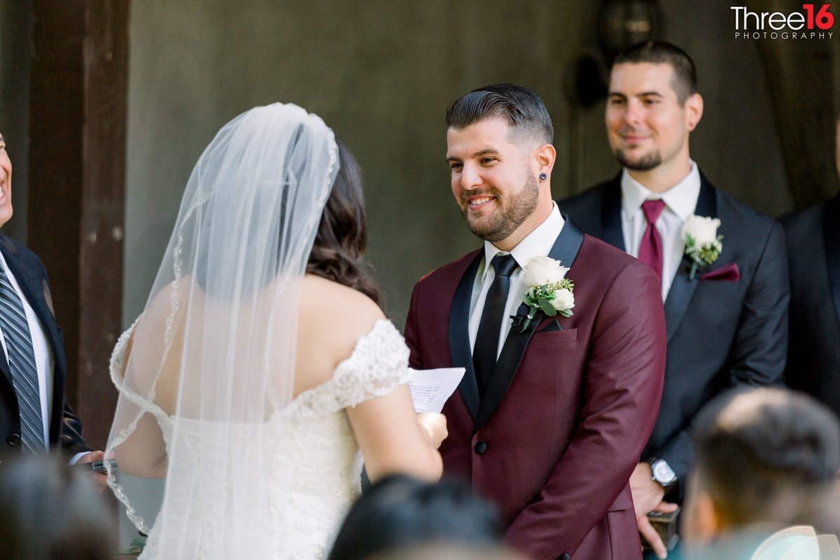 Groom smiles at Bride as she reads him her vows