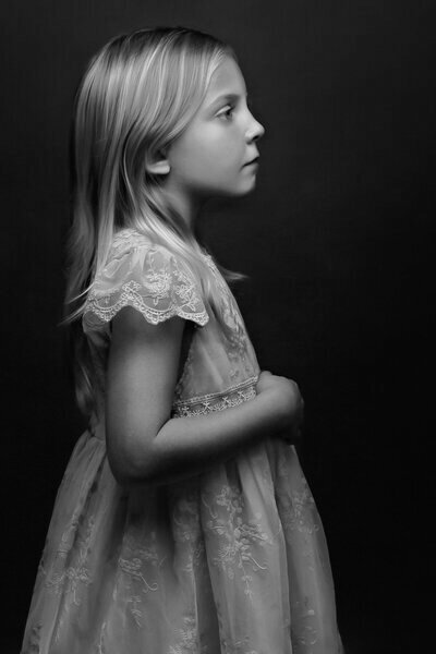 girl child in lace dress standing sideways with right hand mid-chest and face upright sideways