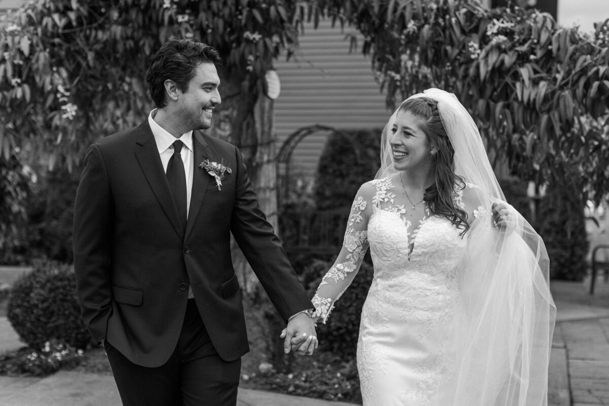 Black-and-white-photo-of-bride-and-groom-laughing-and-walking-at-golden-hour-on-wedding-day-at-Belle-Chapel-in-Snohomish-WA-photo-by-Joanna-Monger-Photography