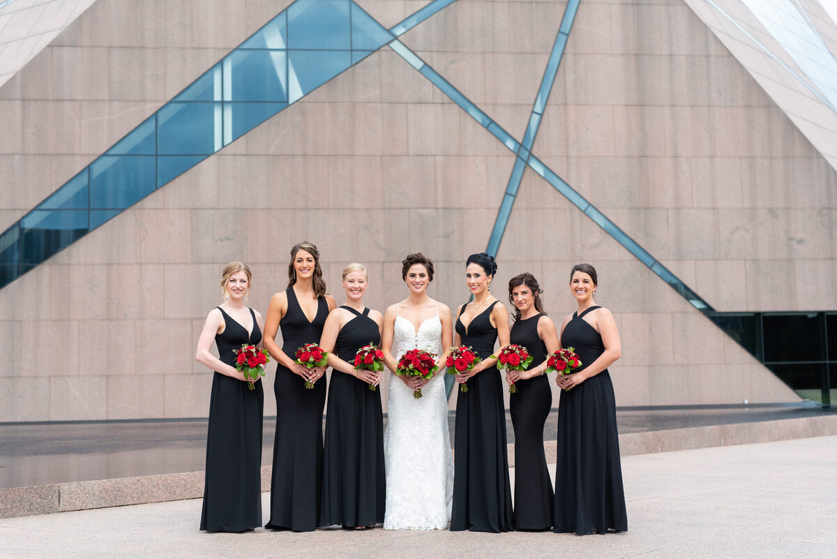 Bride and her bridal party pose together holding red rose bouquets