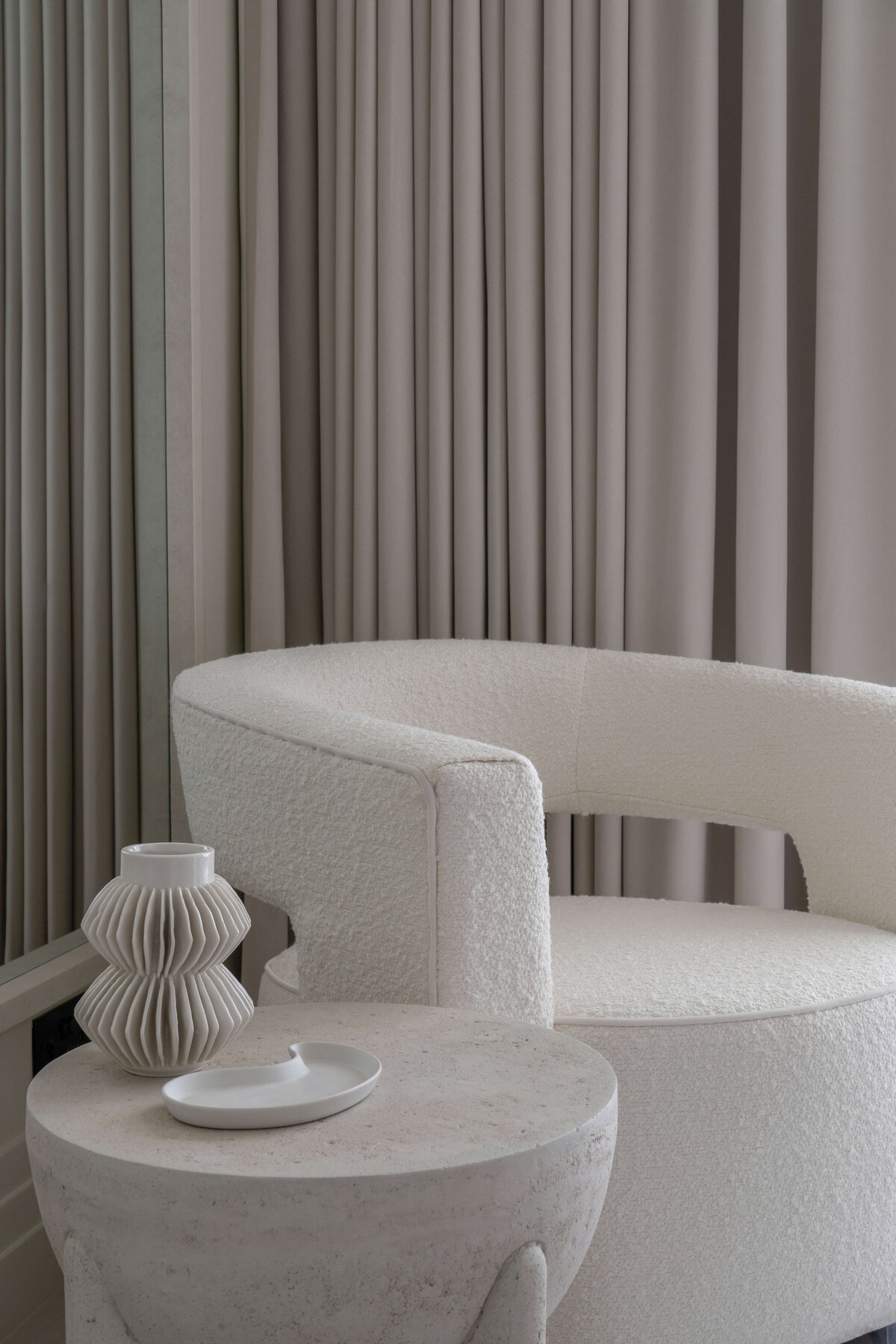 White contemporary armchair in a light and airy guest bedroom. Next to the chair is a sleek stone side table with neutral colored decor.