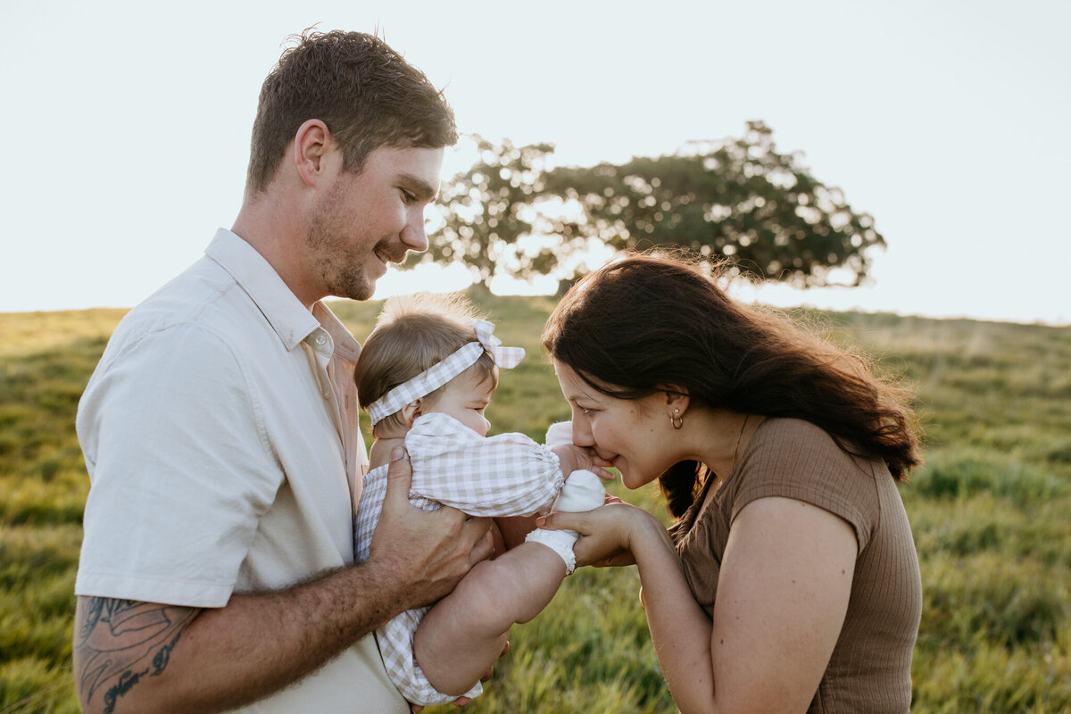 Dad holds their baby as mom tickles her tiny feet, capturing a joyful family moment.