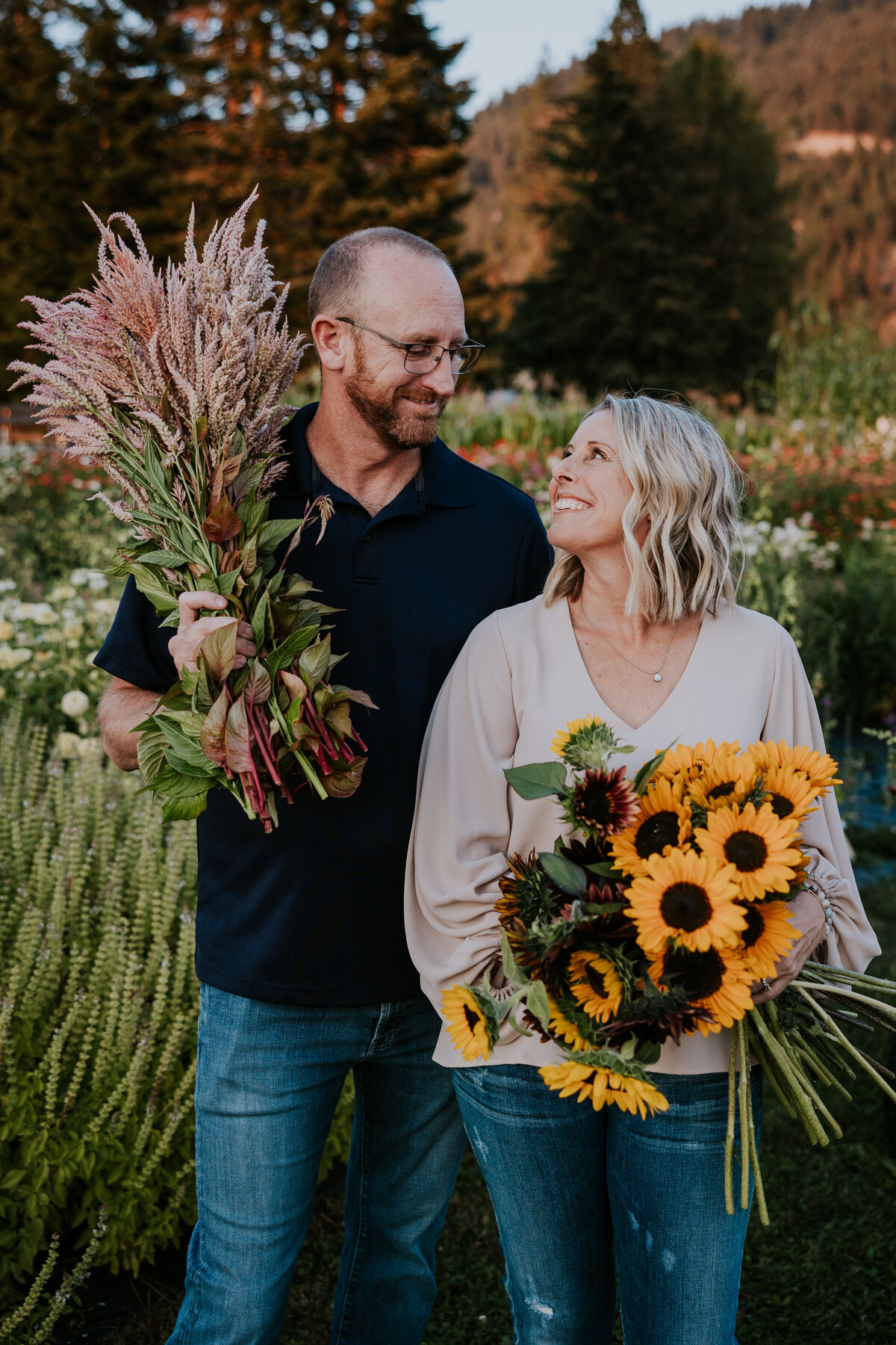 Couple smiles at each other while holding large bundles of flowers.