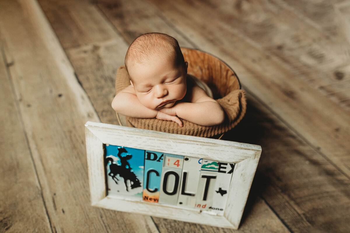 newborn sleeping in a bucket prop with a license plate in front of him