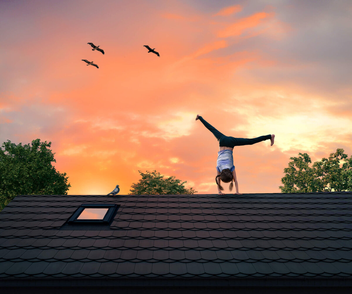 A little girl turning a cartwheel on the roof of a house while birds fly by created by an Asheville Family Photographer