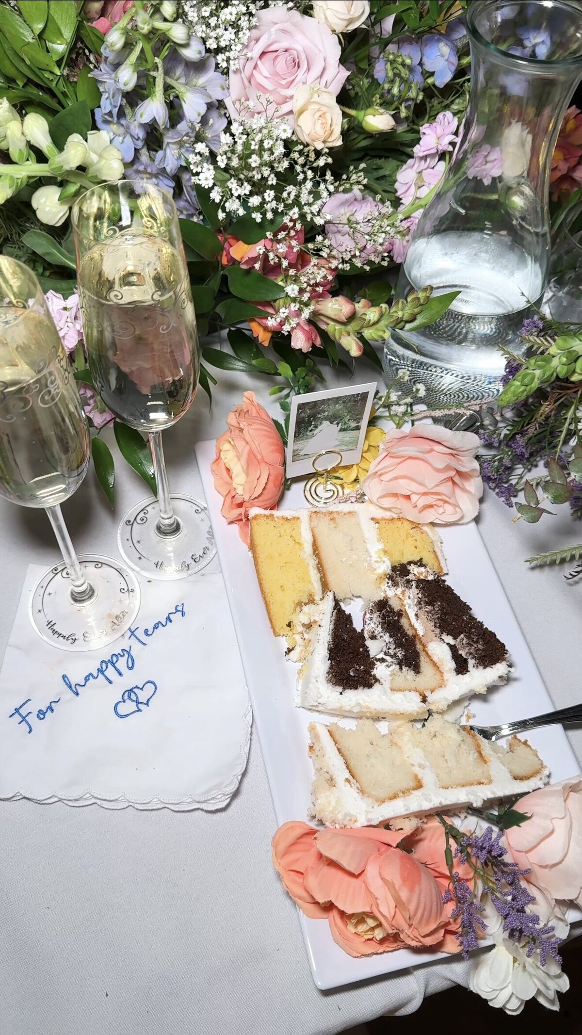 Reception flat lay with flash featuring the cake, champagne, flowers, and hankerchief.
