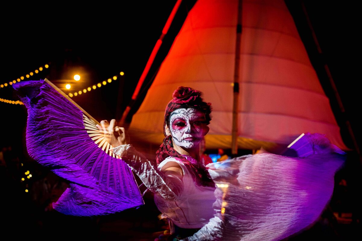 Dancer with Day of the Dead facepaint holds silk fans and dances while staring into the camera. Image shot with blurred motion for artistic feel