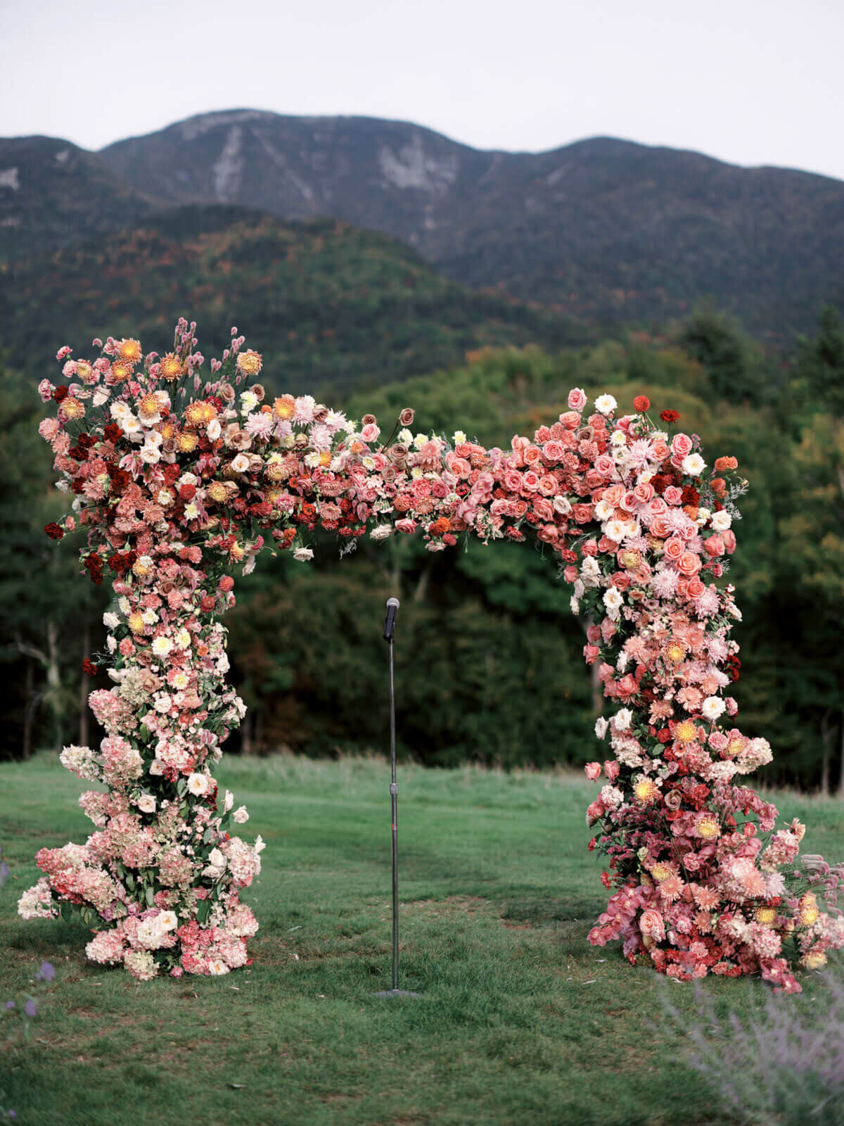 A beautiful wedding arch filled with peach and white flowers, with mountains in the background. Image by Jenny Fu Studio.