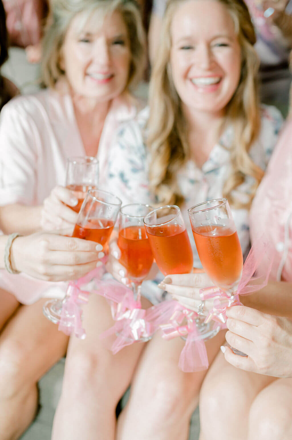 Bridal party toasting one another with glasses that have pink bows tied onto them
