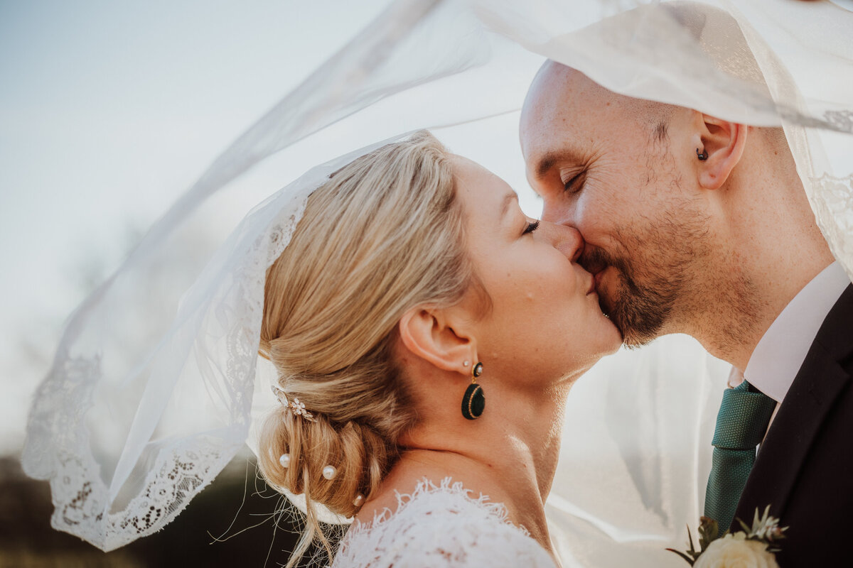 Couple enjoying a kiss under bride's veil t Elcot Park
