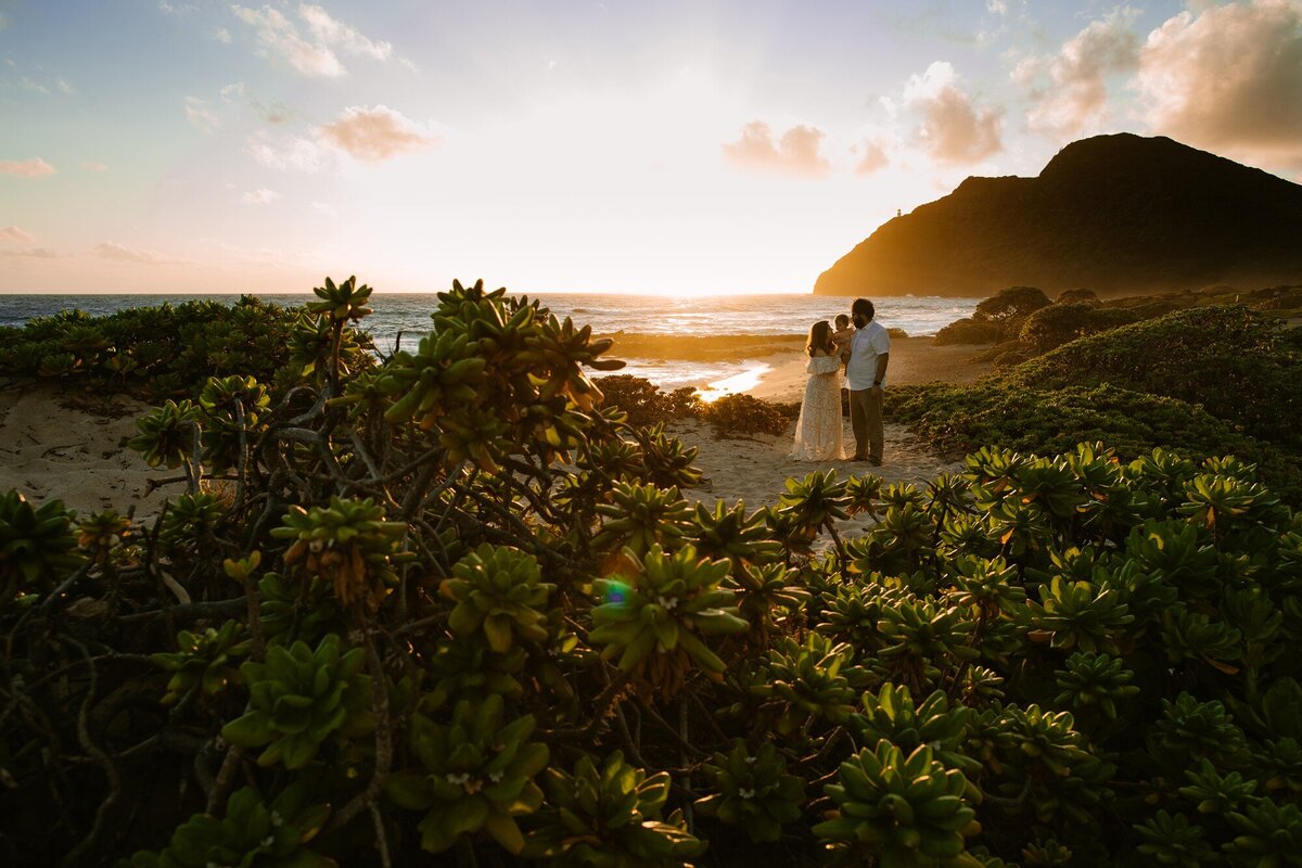 a family of three snuggles at sunrise over makapuu oahu