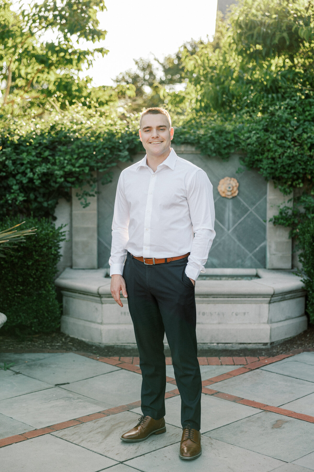 Man with hand in pocket poses in front of stone fountain in Columbus park.