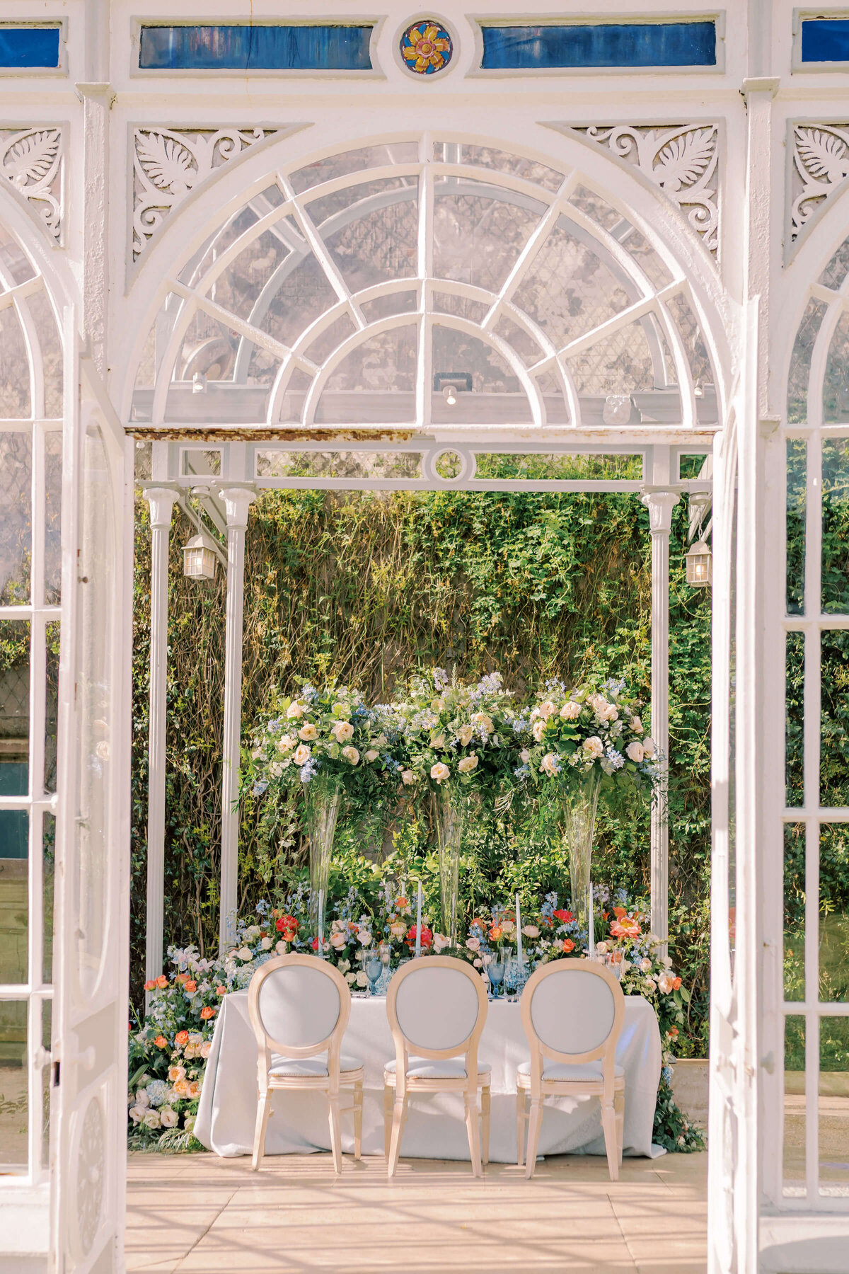 orangery glasshouse at avington park with a blue and coral themed wedding dinner table set up with blue chairs and foliage backdrop behind it