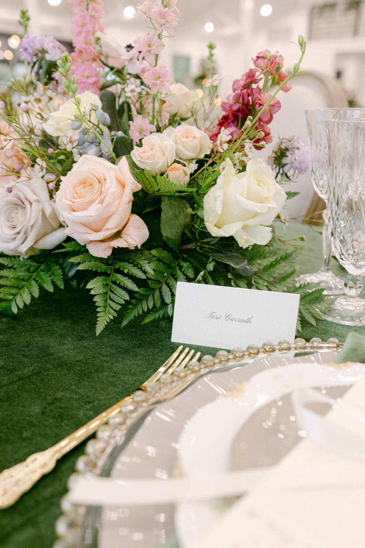 A wedding day photo of the tables in the reception hall that are covered in green linens with florals & candles on top