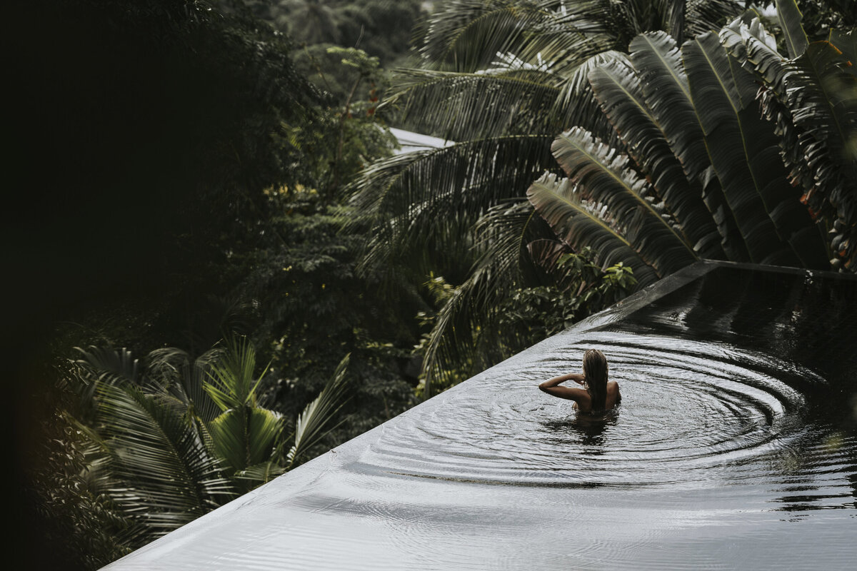 A serene infinity pool overlooking lush tropical greenery at Amanpuri, Thailand, with a traveler relaxing in the tranquil waters.