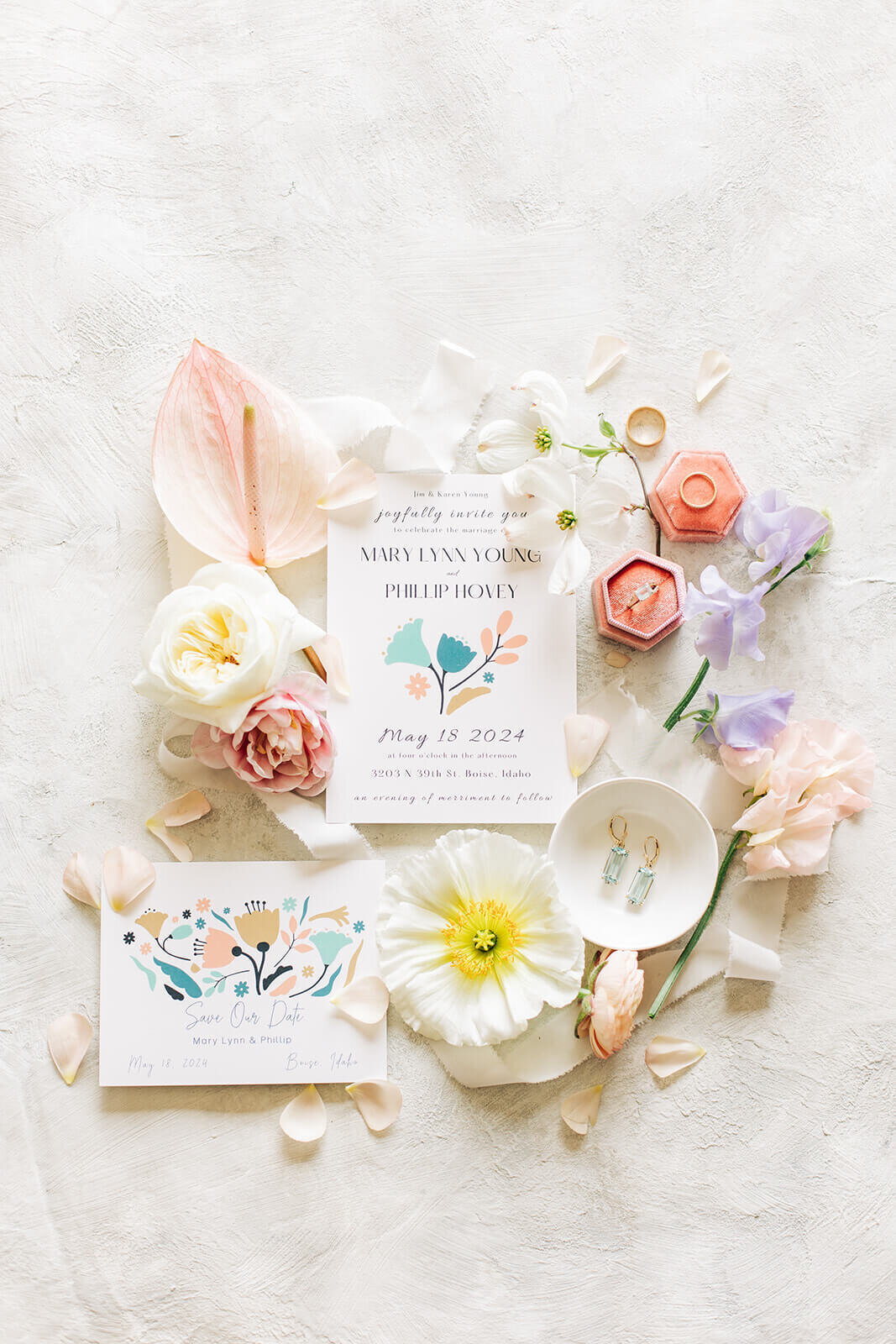 A flat lay of wedding details including invitations, jewelry and flowers.