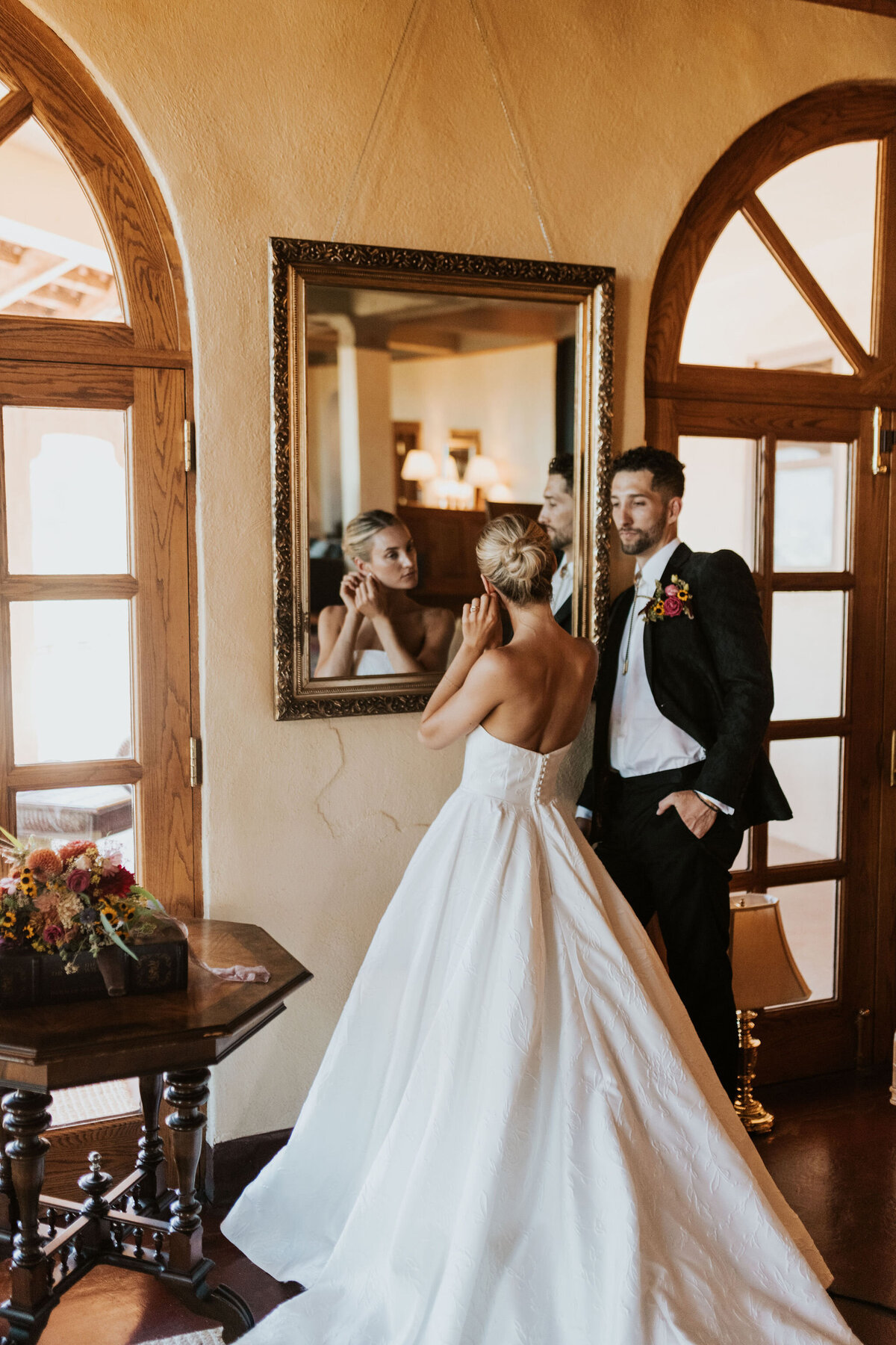 a groom watching a bride put on earrings before their wedding