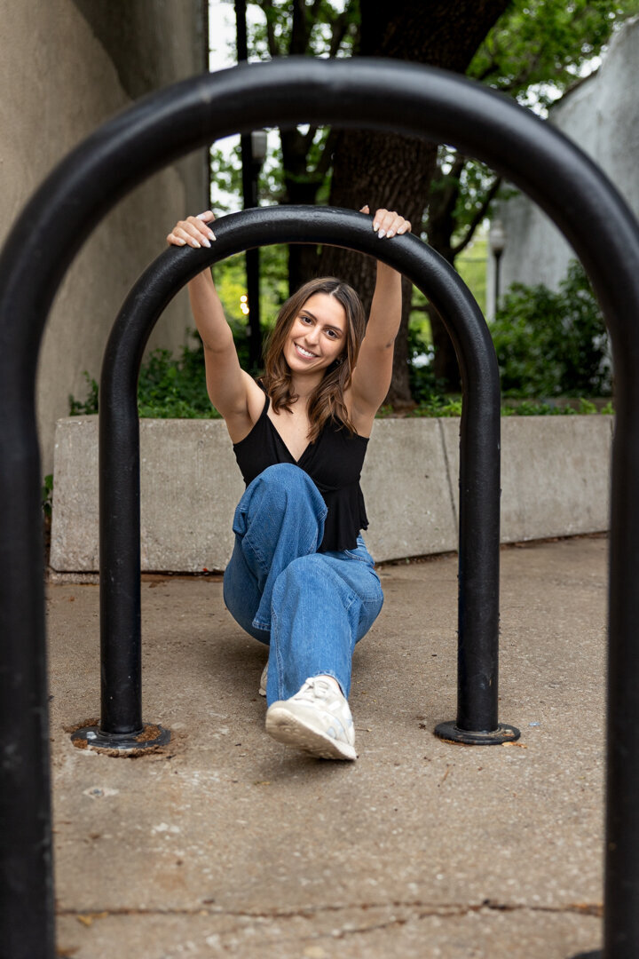 A senior girl peering though and holding onto arches in downtown Lawrence, KS