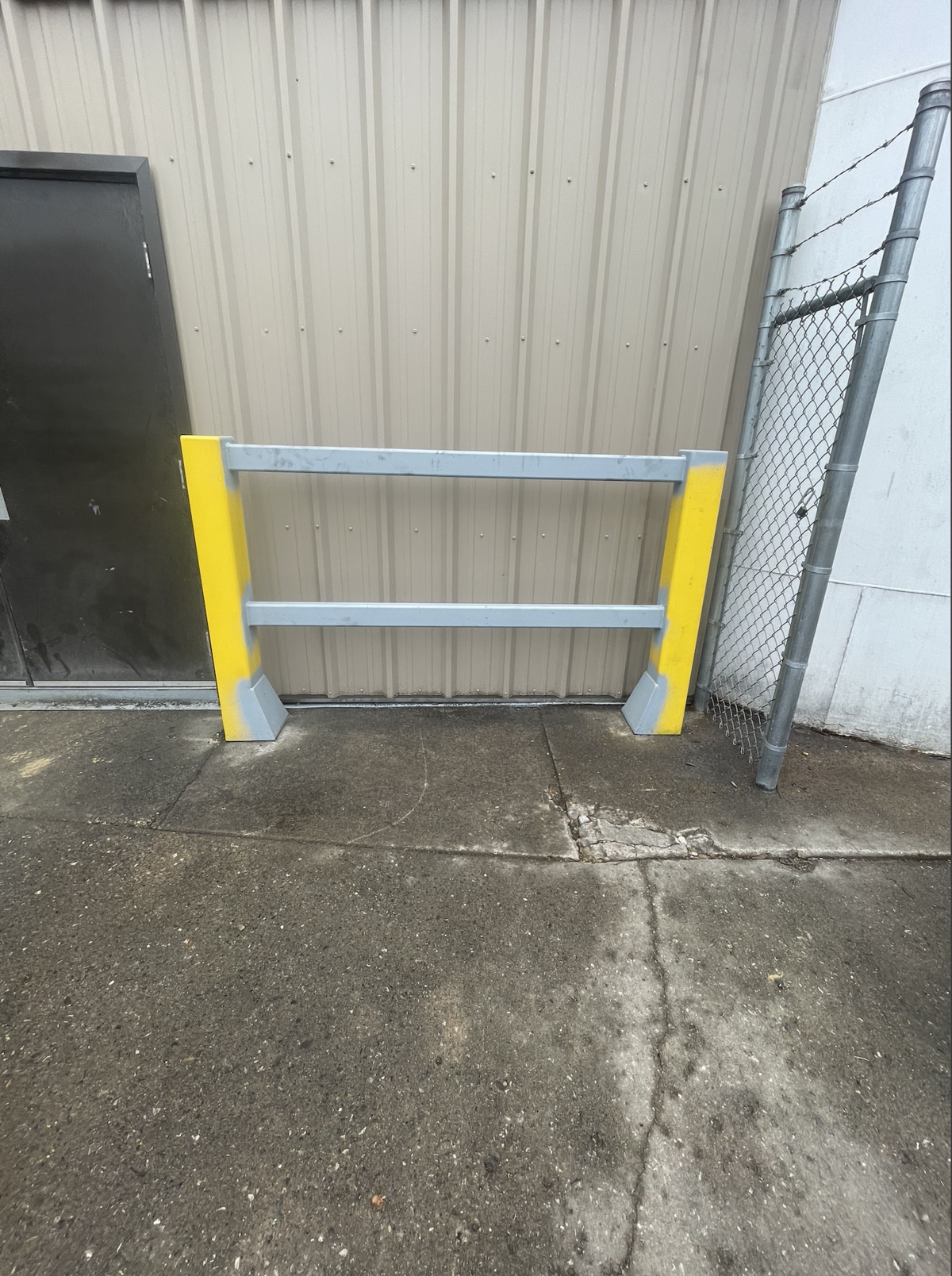 Installed welded steel safety barrier with yellow protective bollards outside a commercial facility.