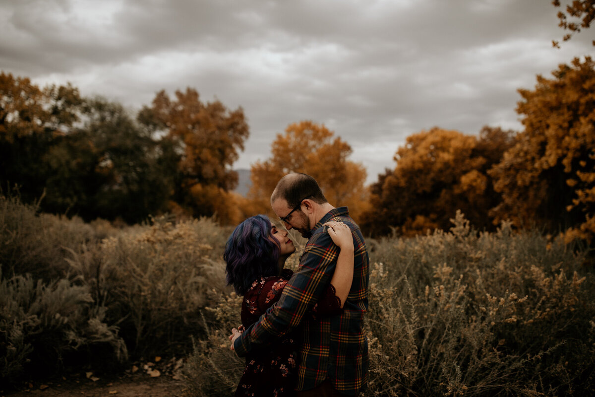 husband and wife holding each other with treed behind them