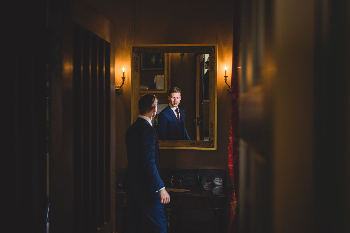 The groom is getting ready at Knowsley hall looking at himself in the mirror