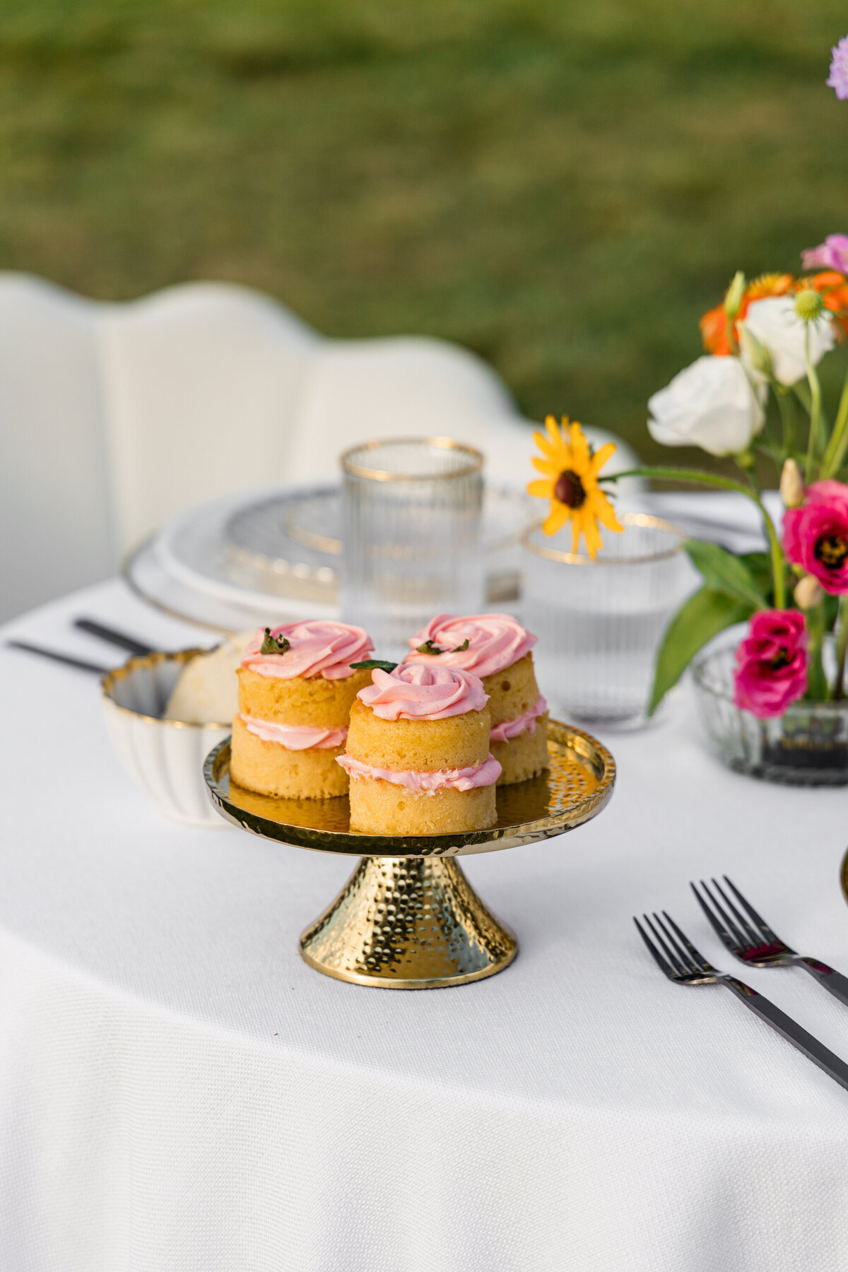 pink orange and white flowers on white table cloth with mixed metal place setting and cupcakes on gold mini cake stand