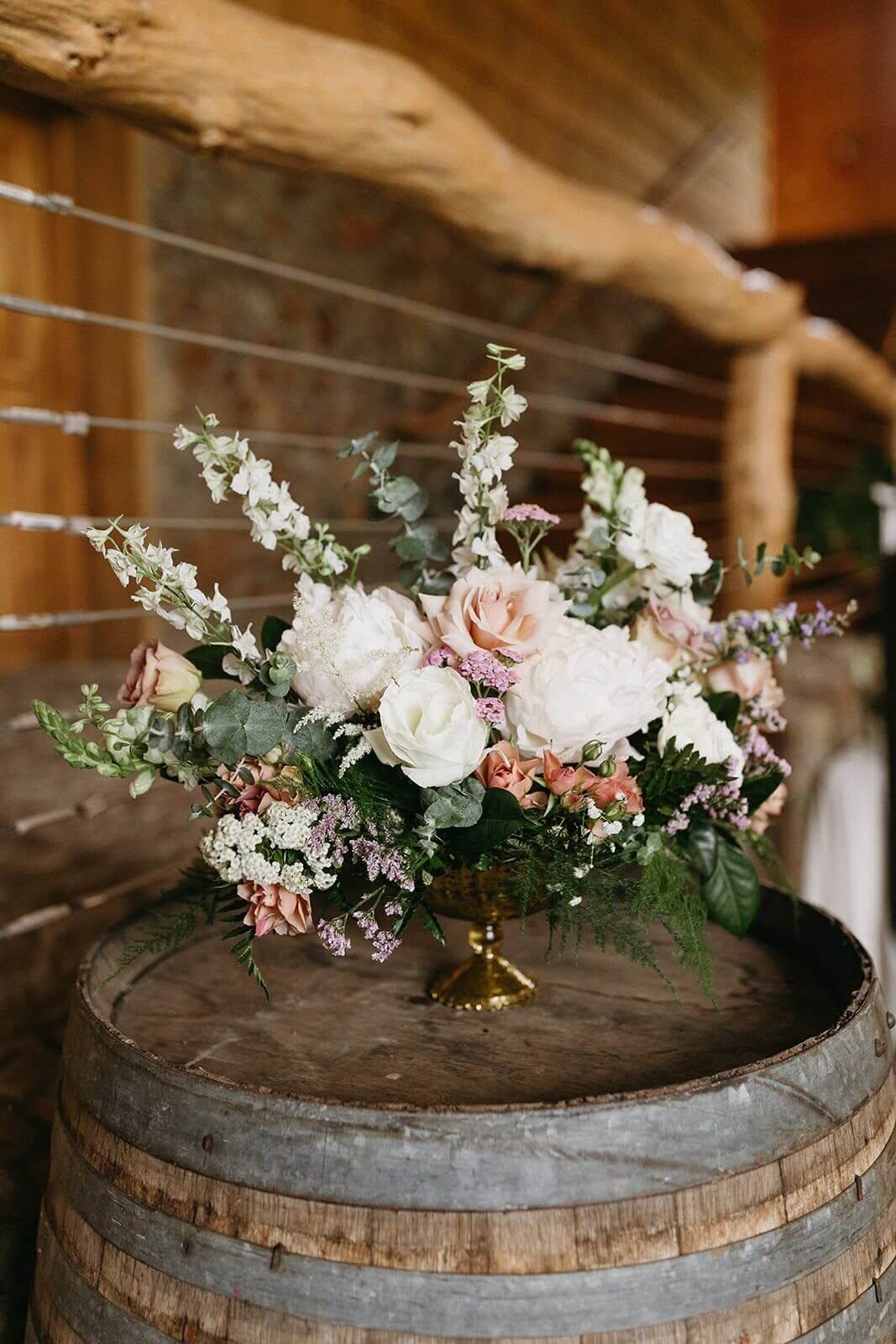A large floral centerpiece sits atop a wine barrel.
