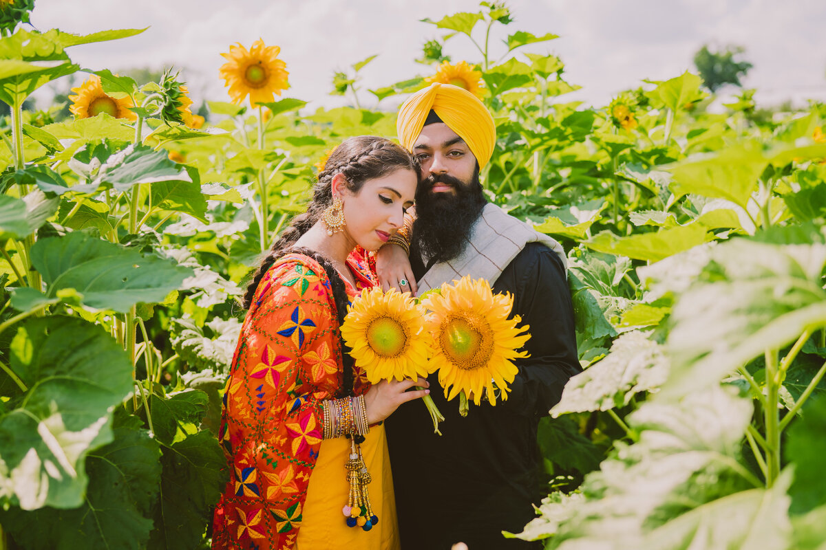 An engaged couple holding sunflowers in traditional Punjabi clothing at a sunflower farm in new jersey