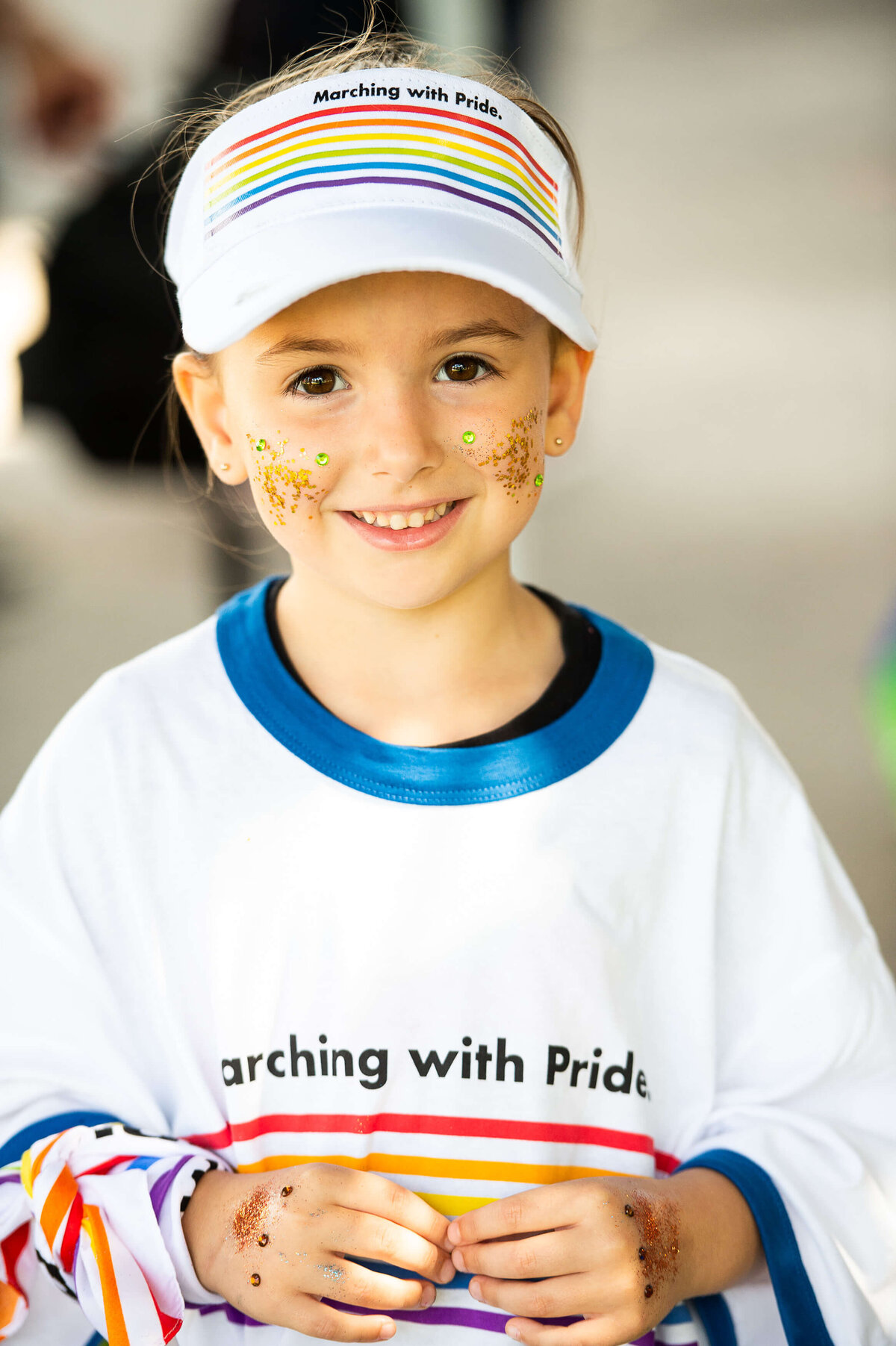 A photo of a smiling child wearing face makeup, a pride t-shirt and visor.  Captured by Ottawa Event Photographer JEMMAN Photography COMMERCIAL during the Tweed Canopy Growth Pride Parade