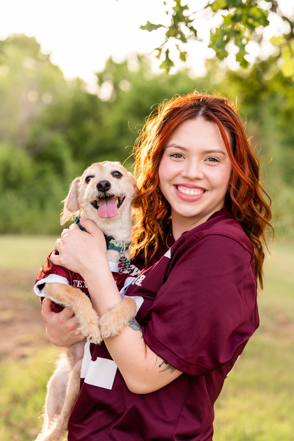 Texas A&M senior girl holding dog and smiling while both wearing maroon jerseys in Leaching Teaching Gardens