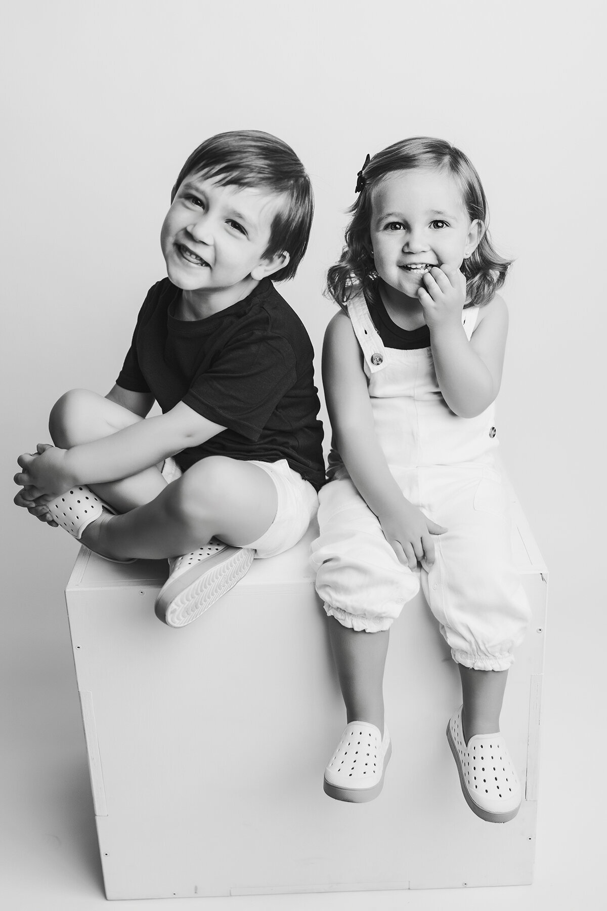 Brother and sister sitting on a box in a black and white photo