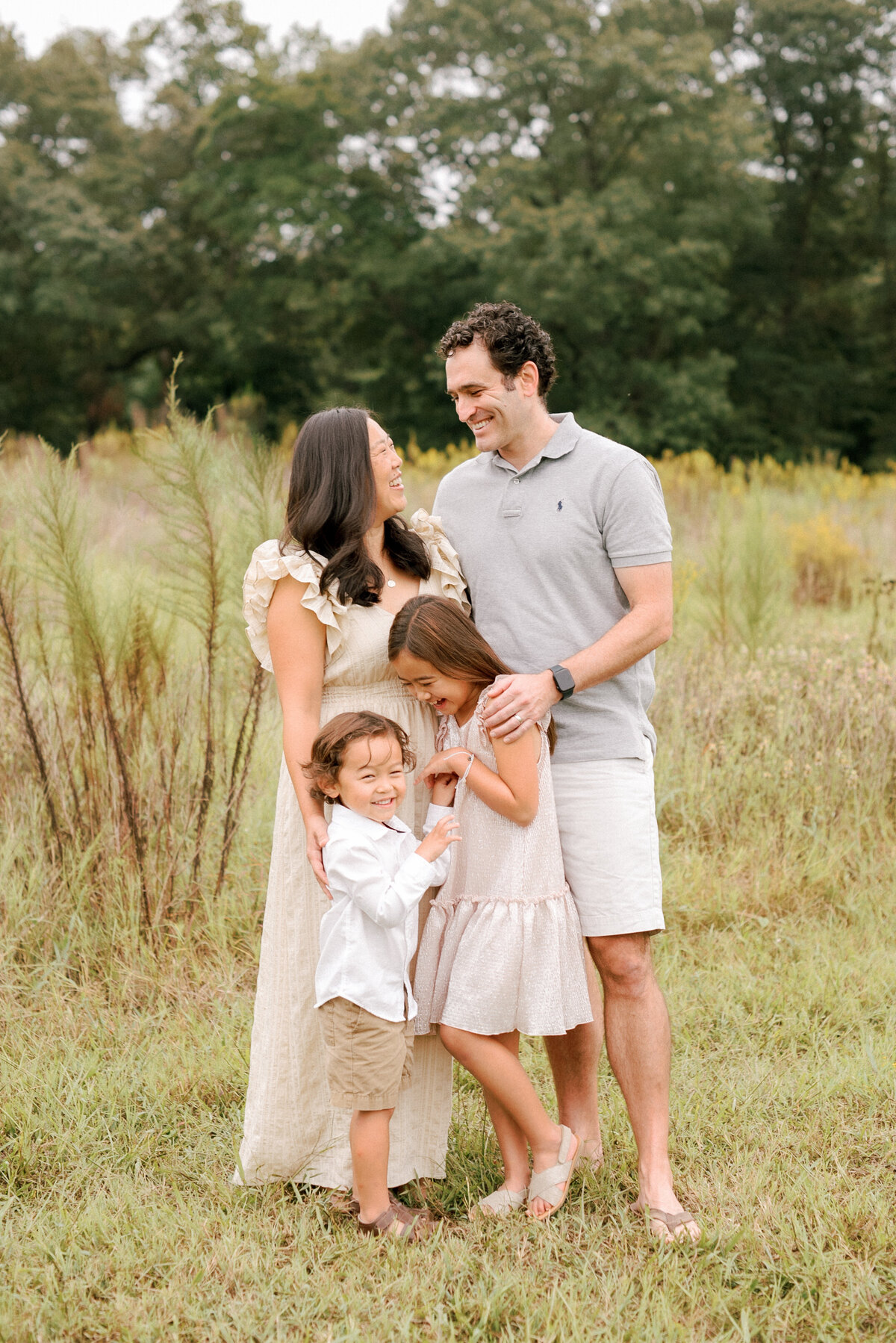 Family laughing and embracing in a field during their Raleigh family session. Photographed by Raleigh Family Photographer A.J. Dunlap Photography