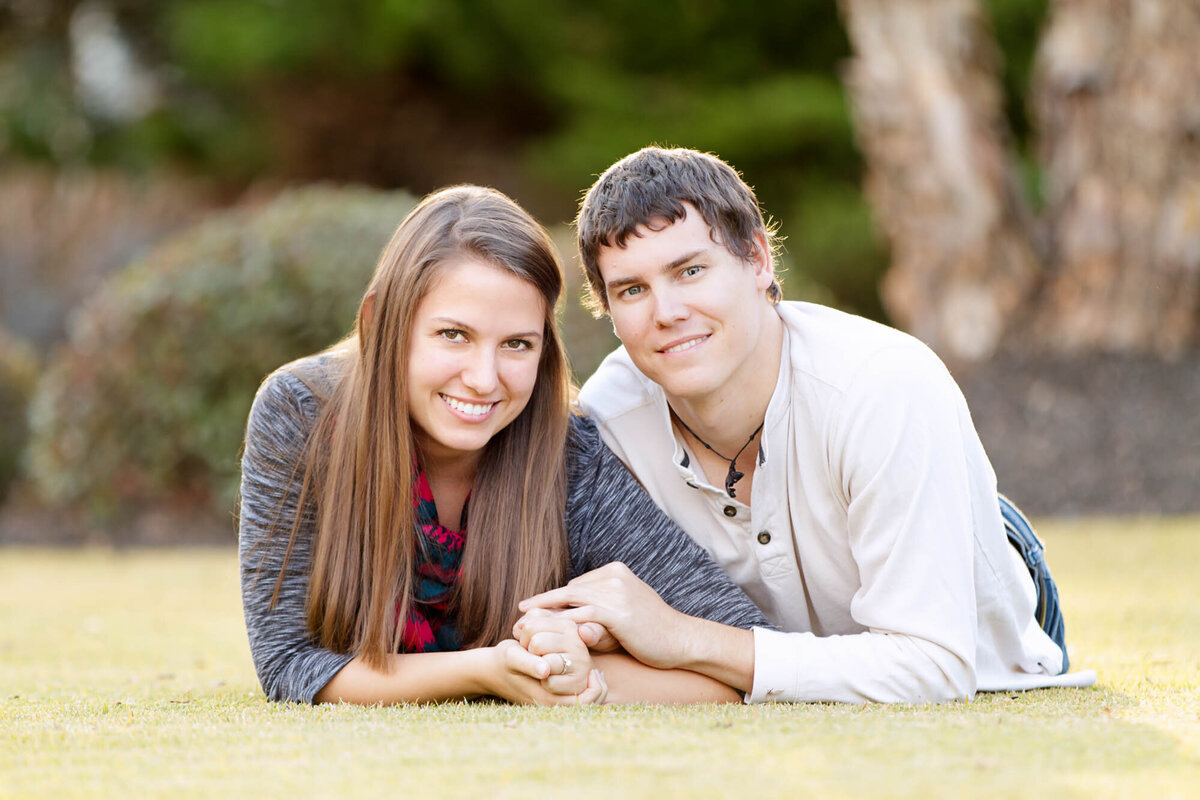 Engagement portrait of a couple lying down in the grass holding hands.