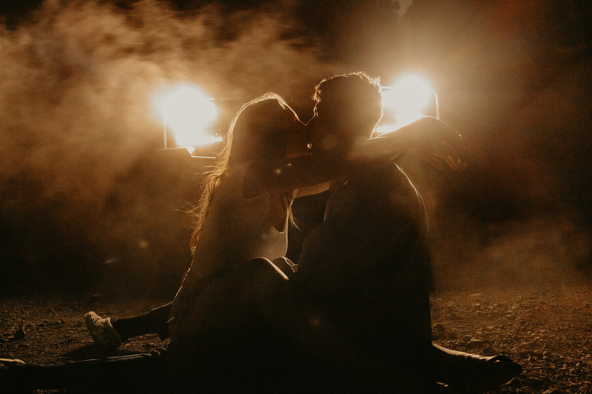 Couple kissing at night with bright lights behind them
