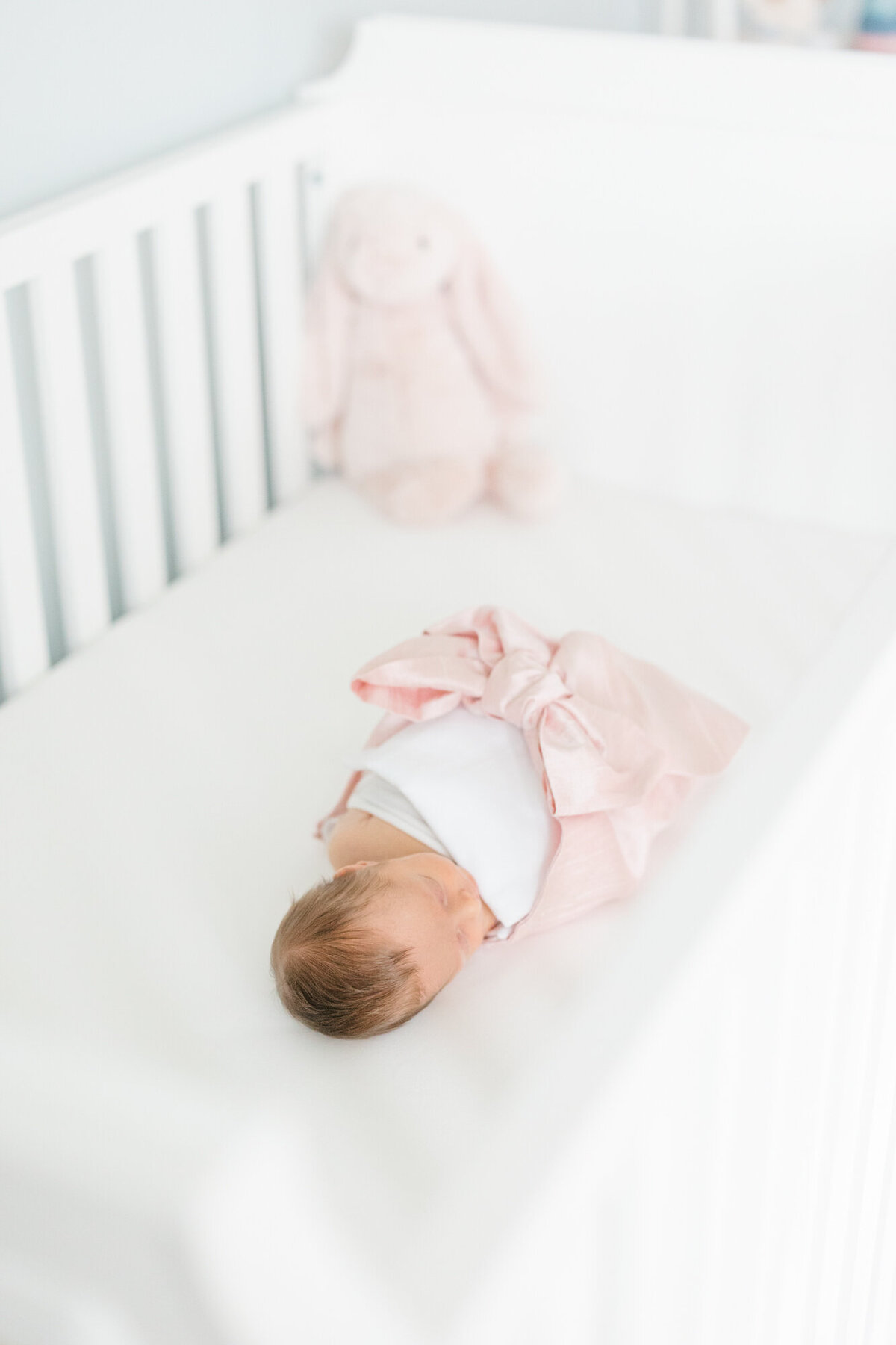 Newborn swaddled in a Beaufort Bonnet Company pink bow swaddle in her crib