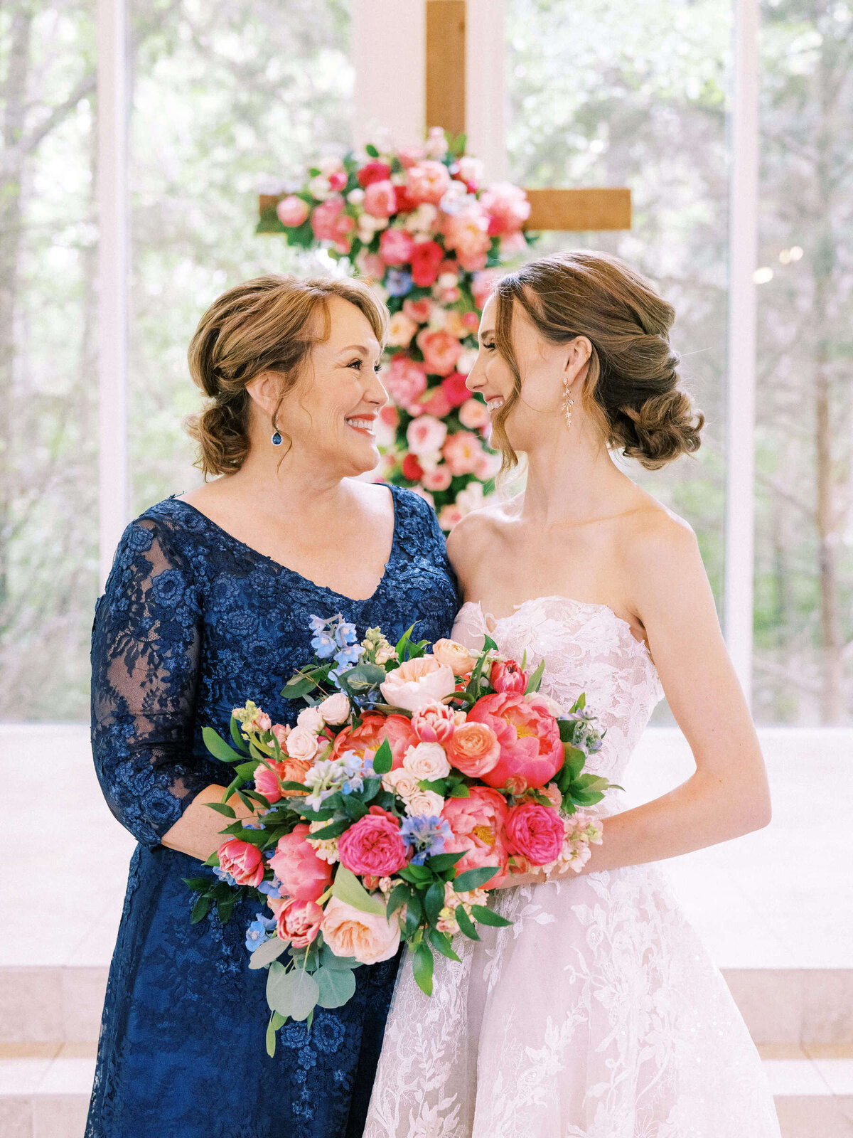 Mother of the bride and bride in lace dresses smile at each other at colorful Ashton Gardens wedding
