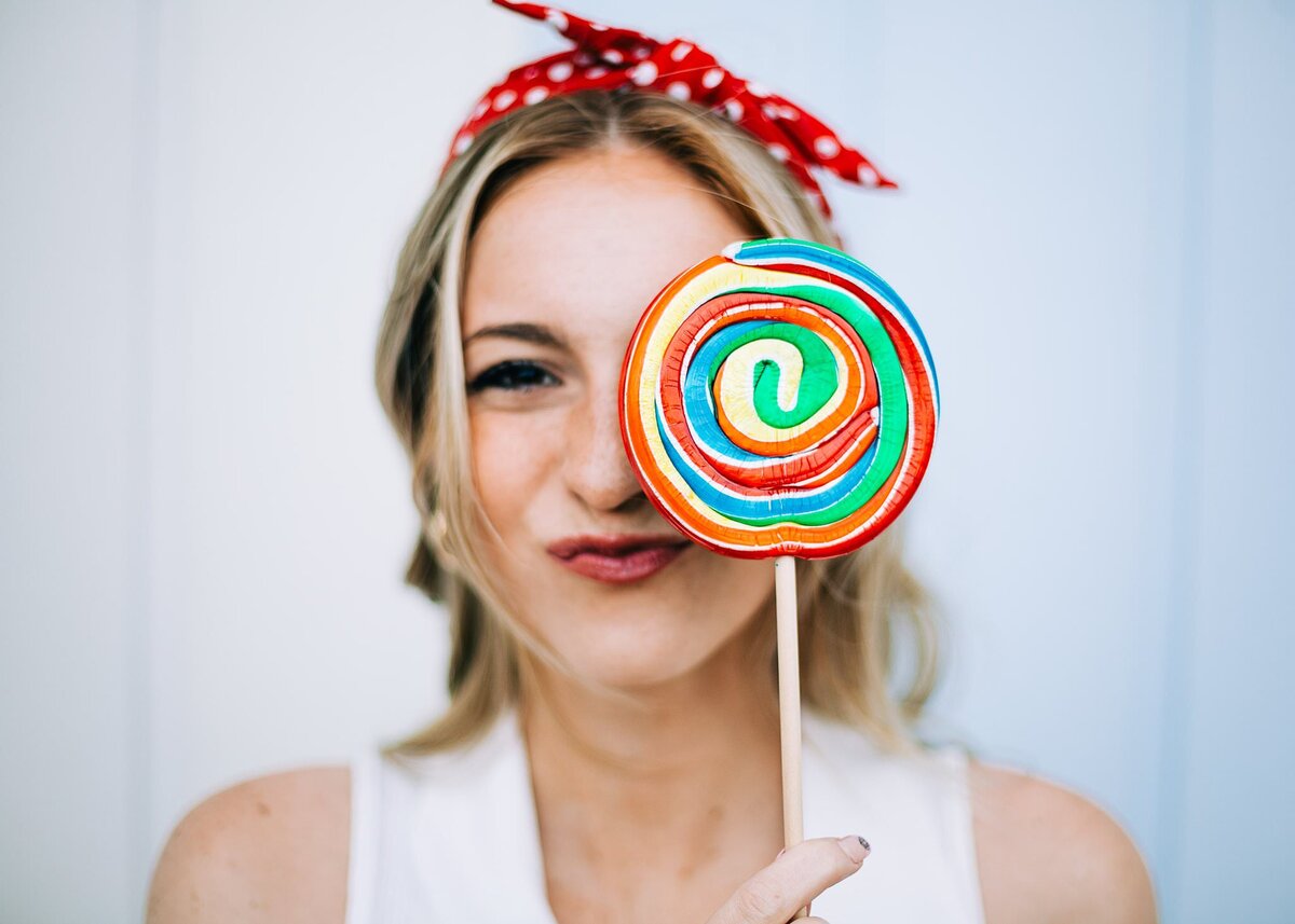 Girl holding a big lollipop in front of her eye, making a funny face