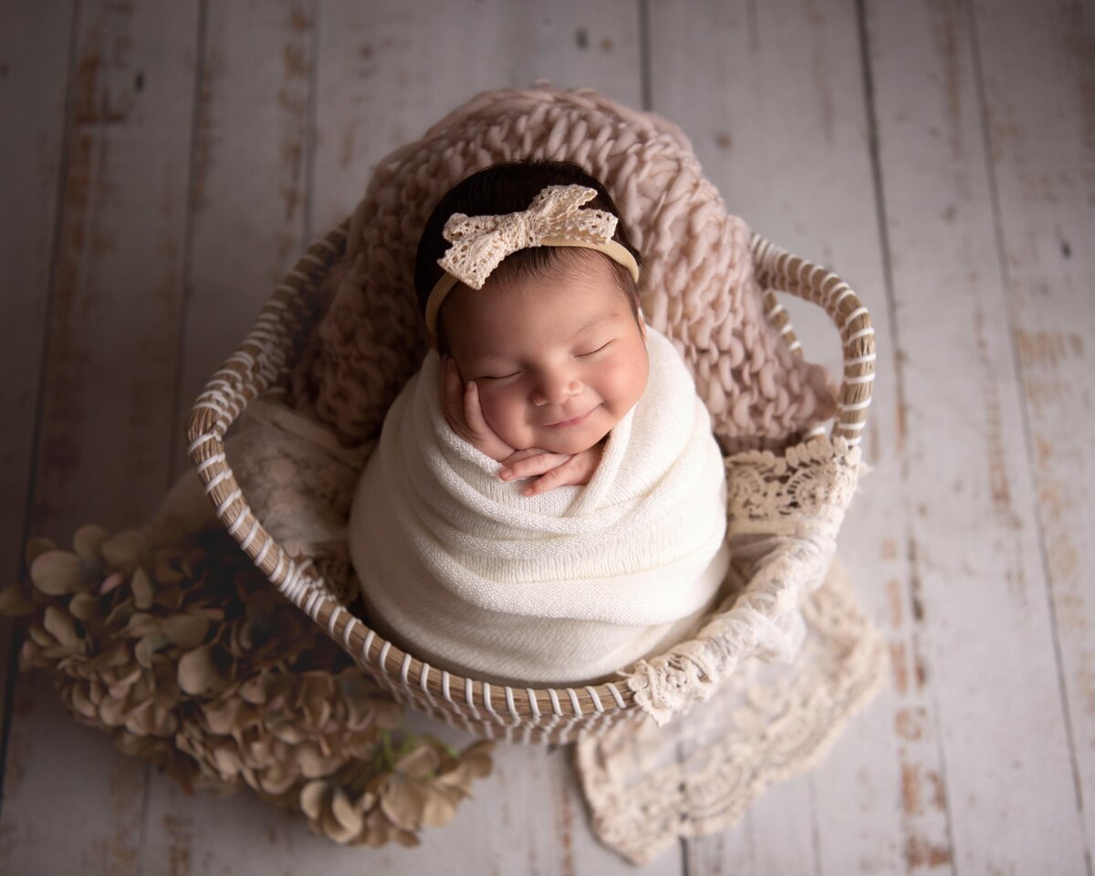 Best Newborn Photographer California | Styled newborn photo | Sleeping, smiling baby in basket with hand on cheek.