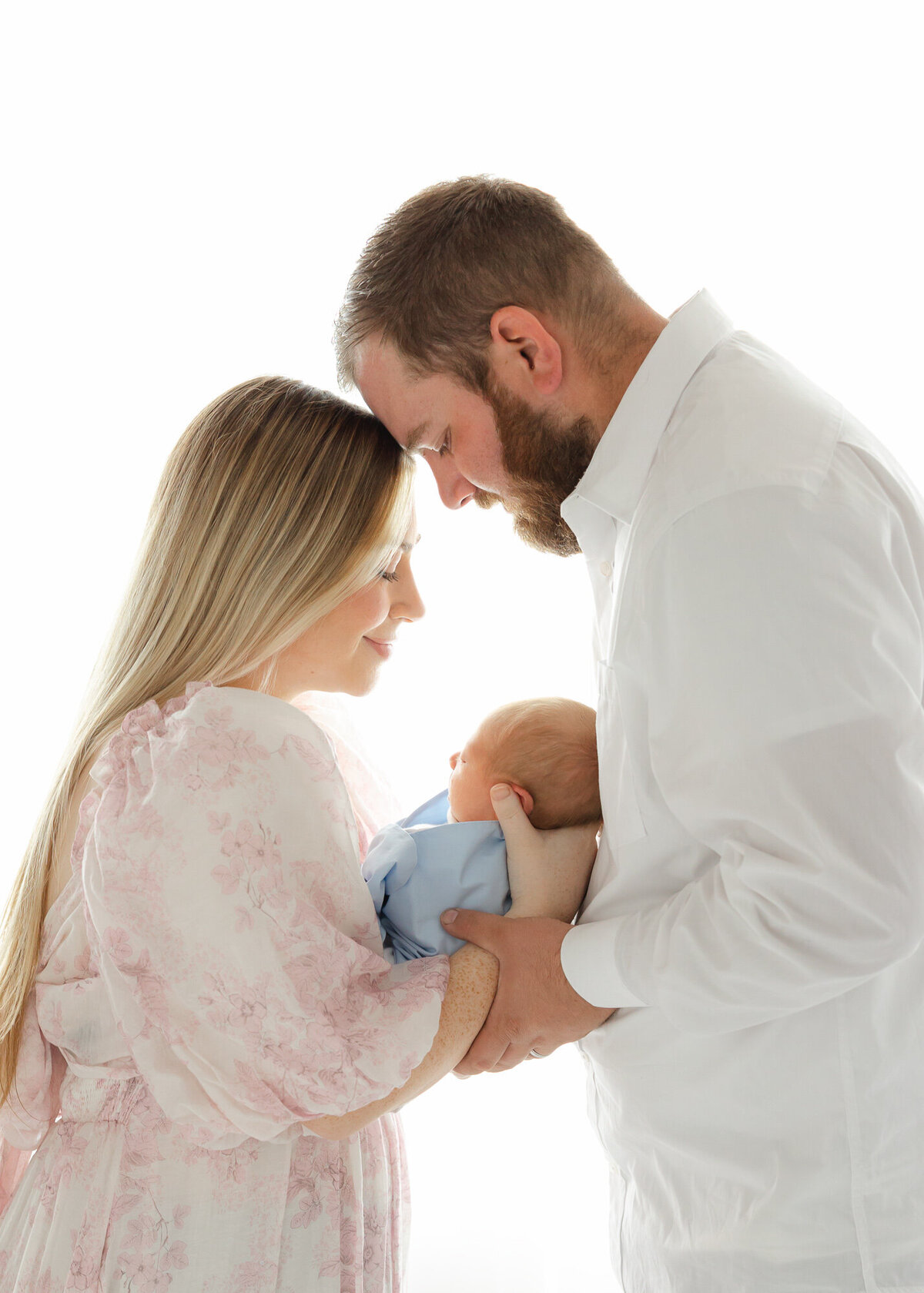 Proud mom and dad holding baby boy who is wrapped in a blue The Beaufort bonnet company wrap. Mom is wearing a dress provided by Constance Calton Photography