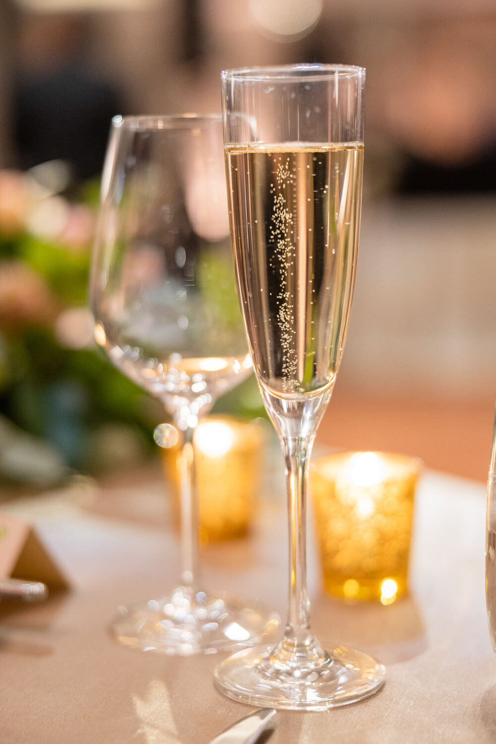 Two glasses of champagne on a table with candles in the background