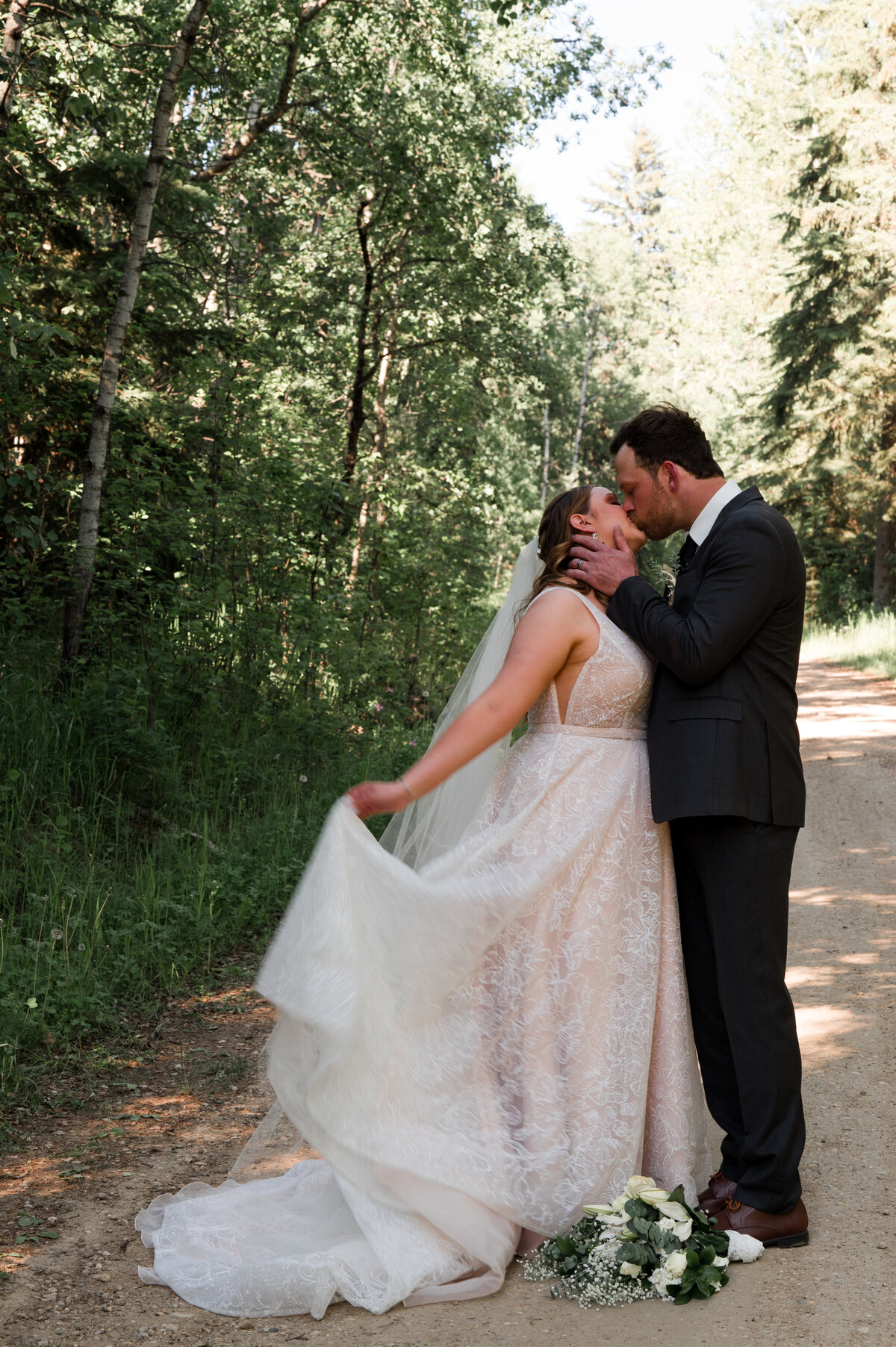 bride and groom on a dirt road stand facing each other and kiss