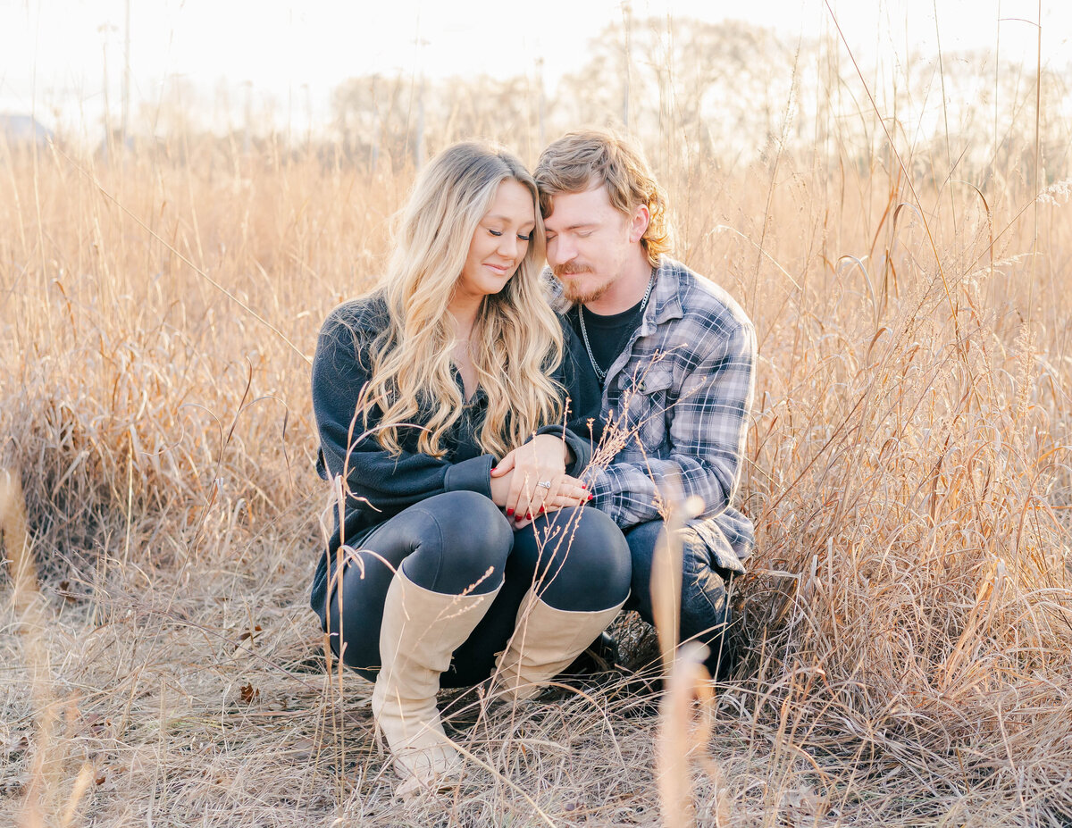married couple sitting in field having a special moment with their eyes closed